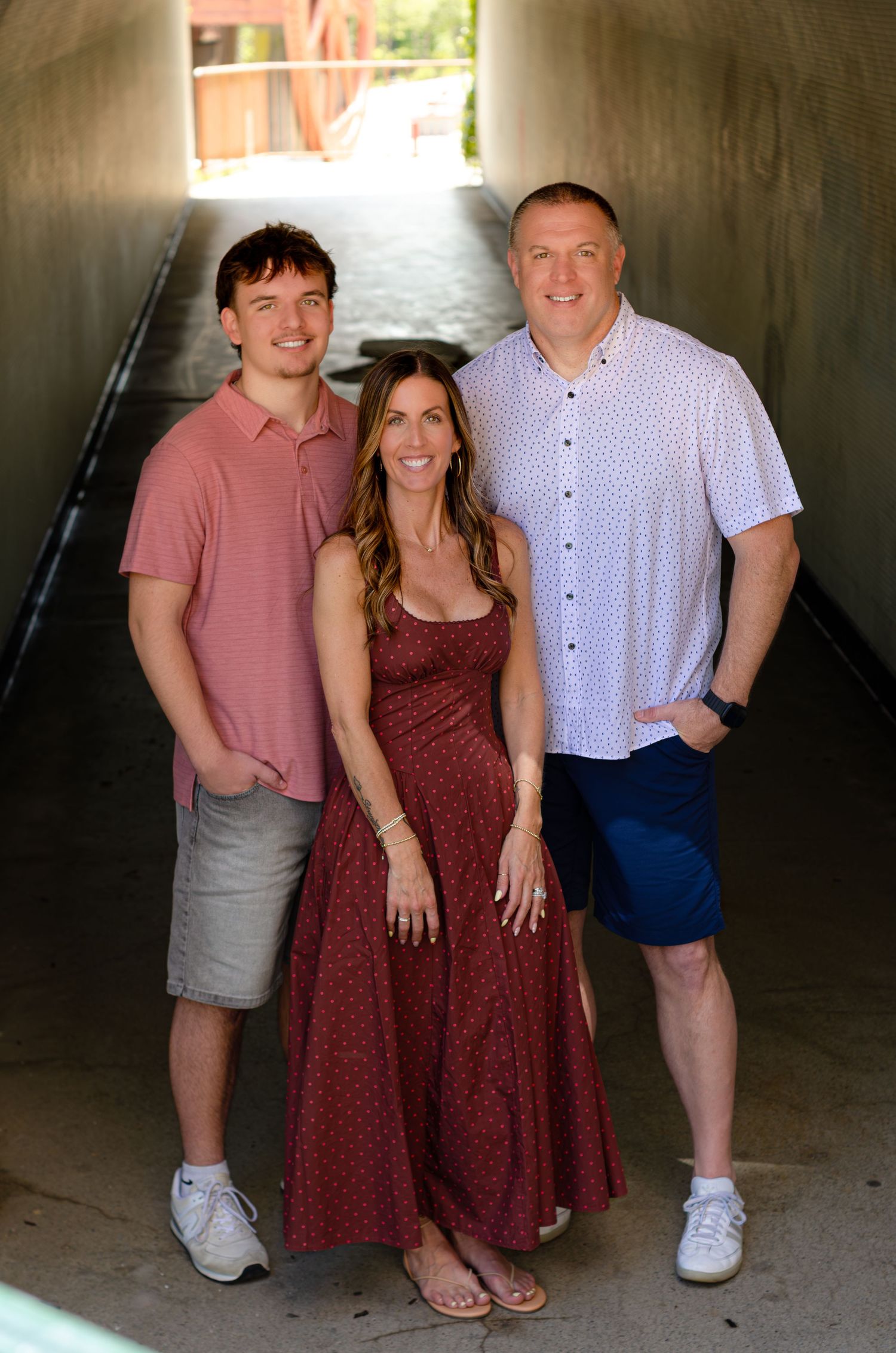 Three smiling people pose together in a tunnel, wearing casual summer outfits in coordinating red and white tones.