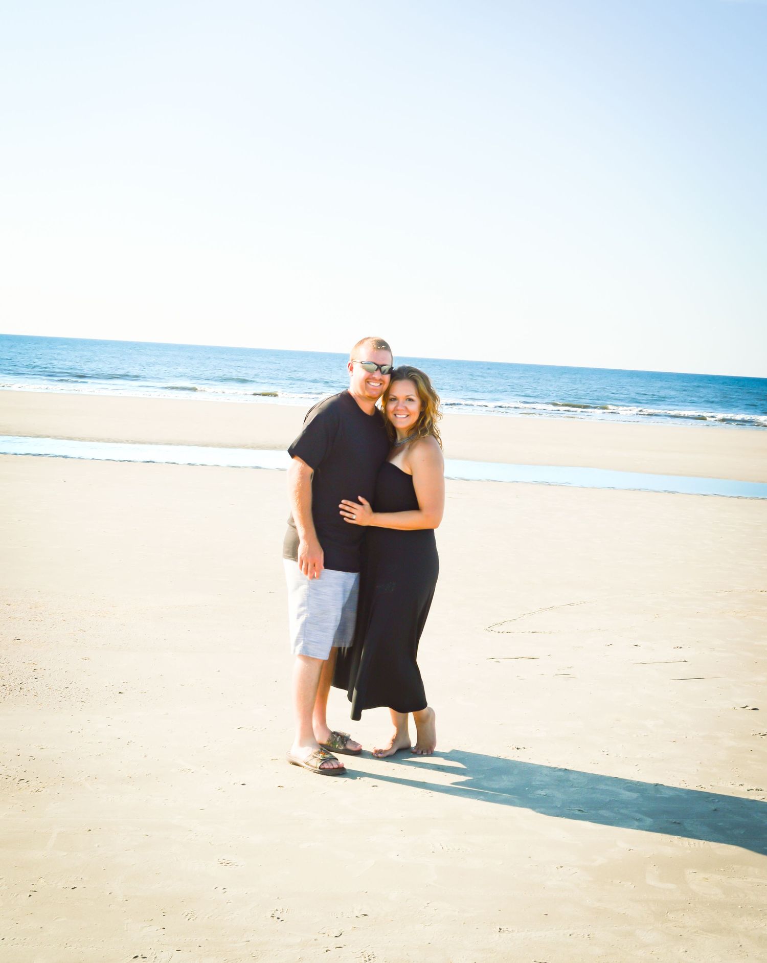 Family embracing on empty beach with ocean waves and bright sunlight in background.