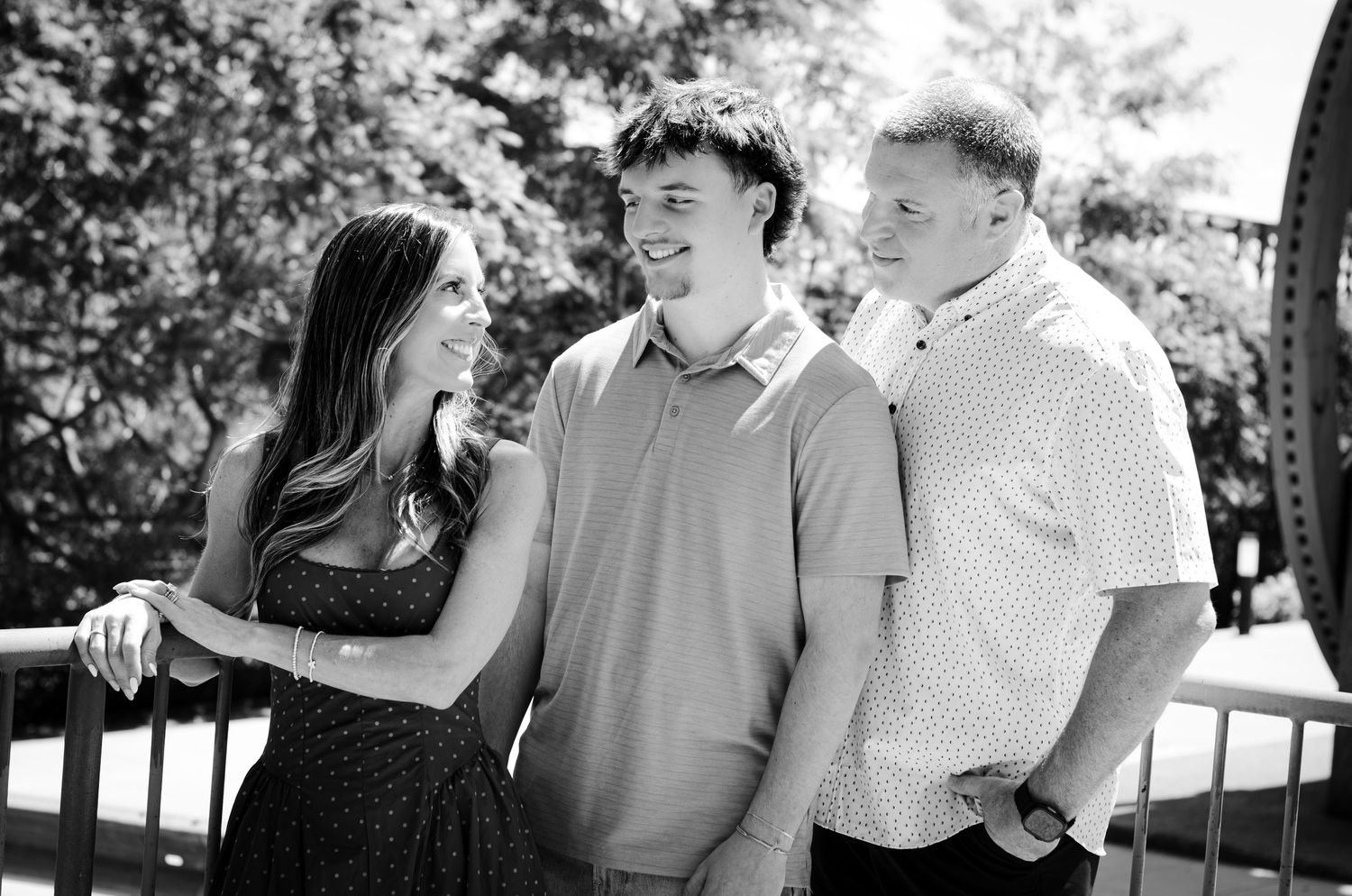 Black and white photo of two young men and a woman smiling together outdoors near a railing.