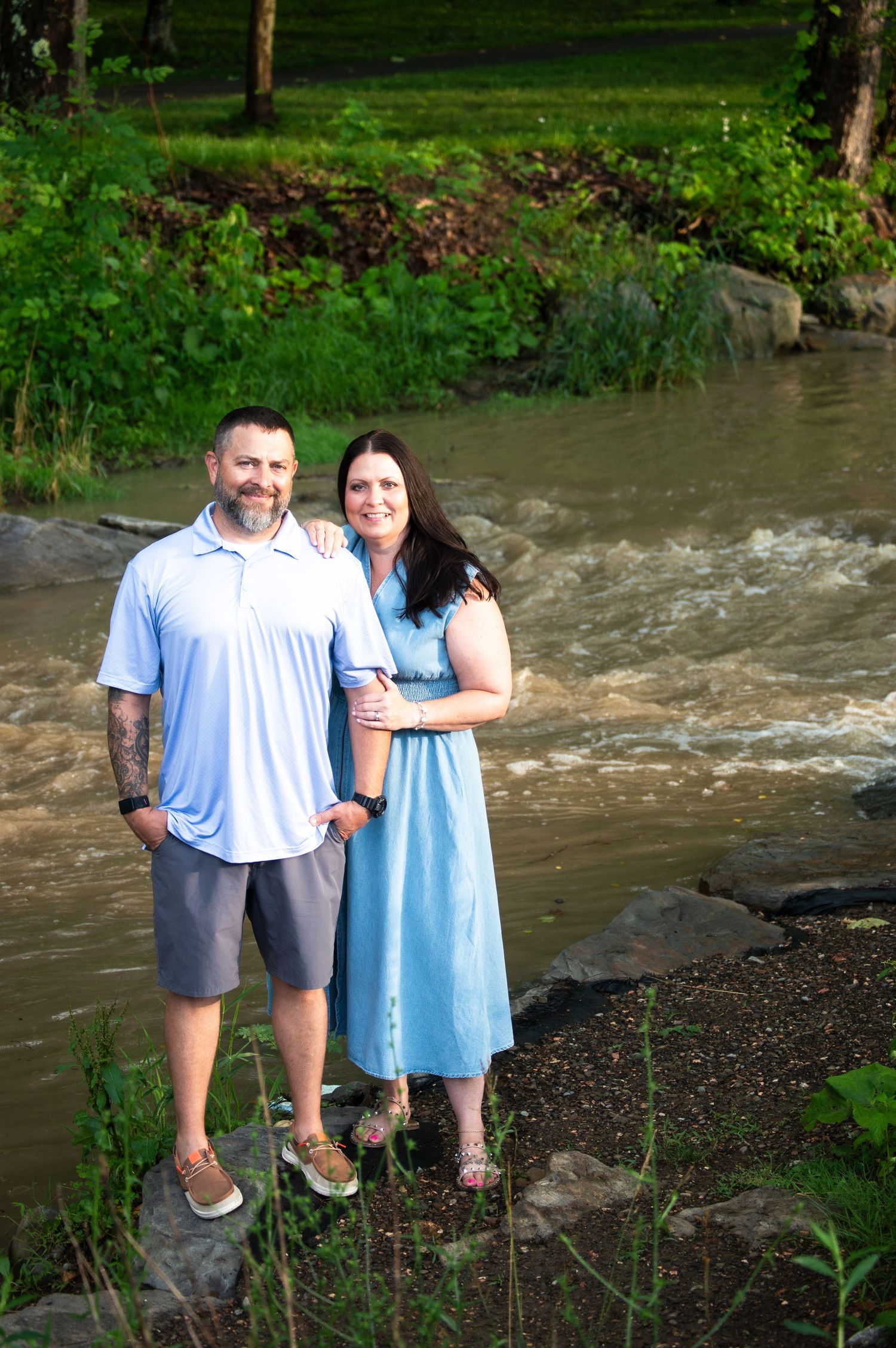 Couple standing together by rushing stream in a wooded setting.