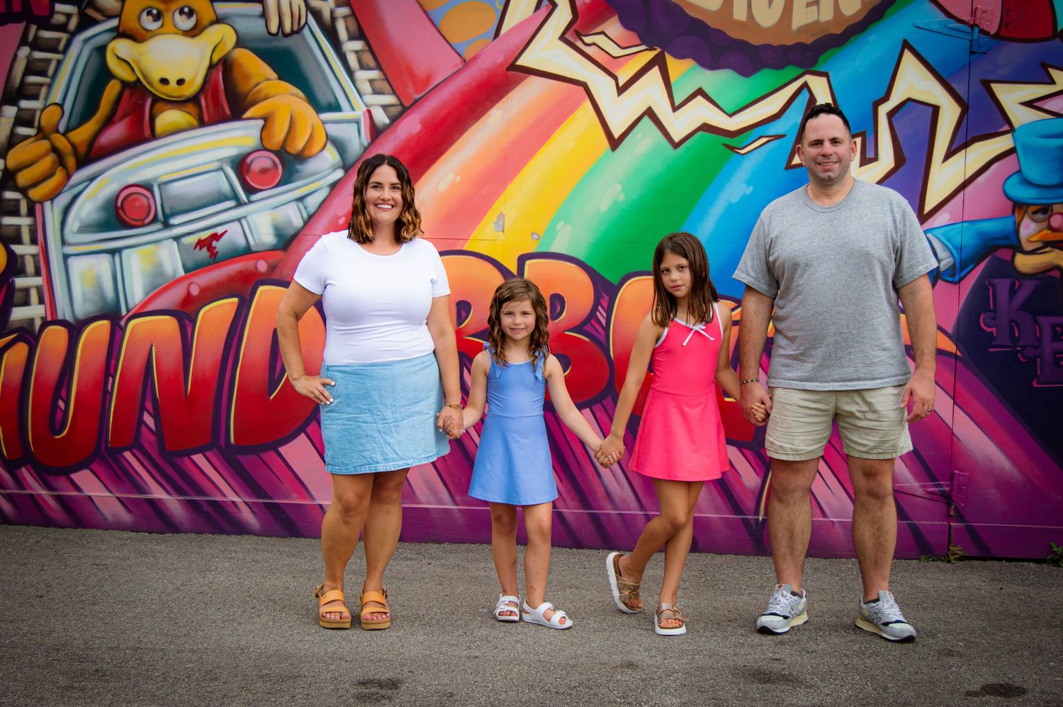 Family of four posing in front of colorful graffiti mural at amusement park.