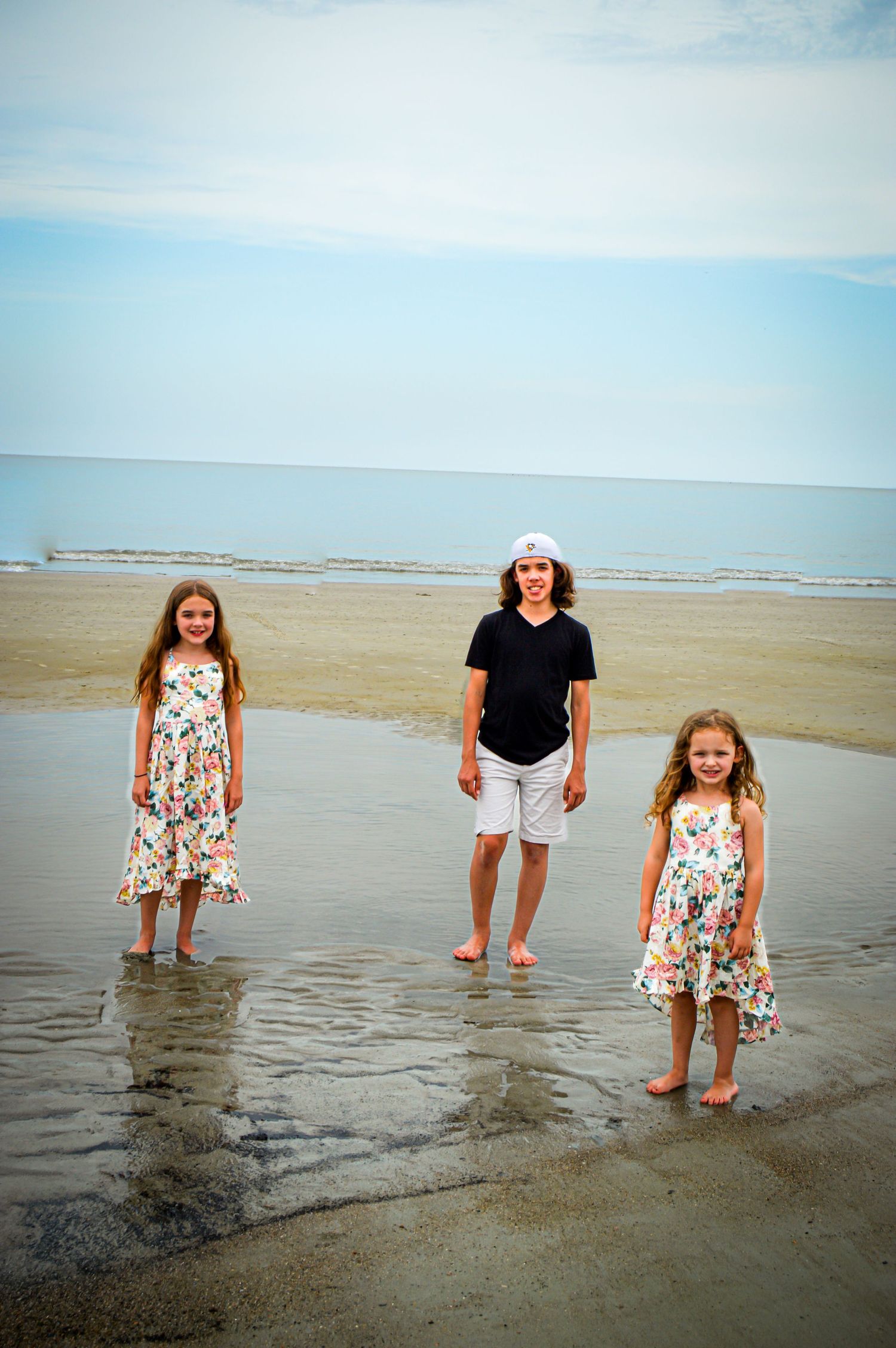 Three people pose in matching outfits while standing in shallow beach water.