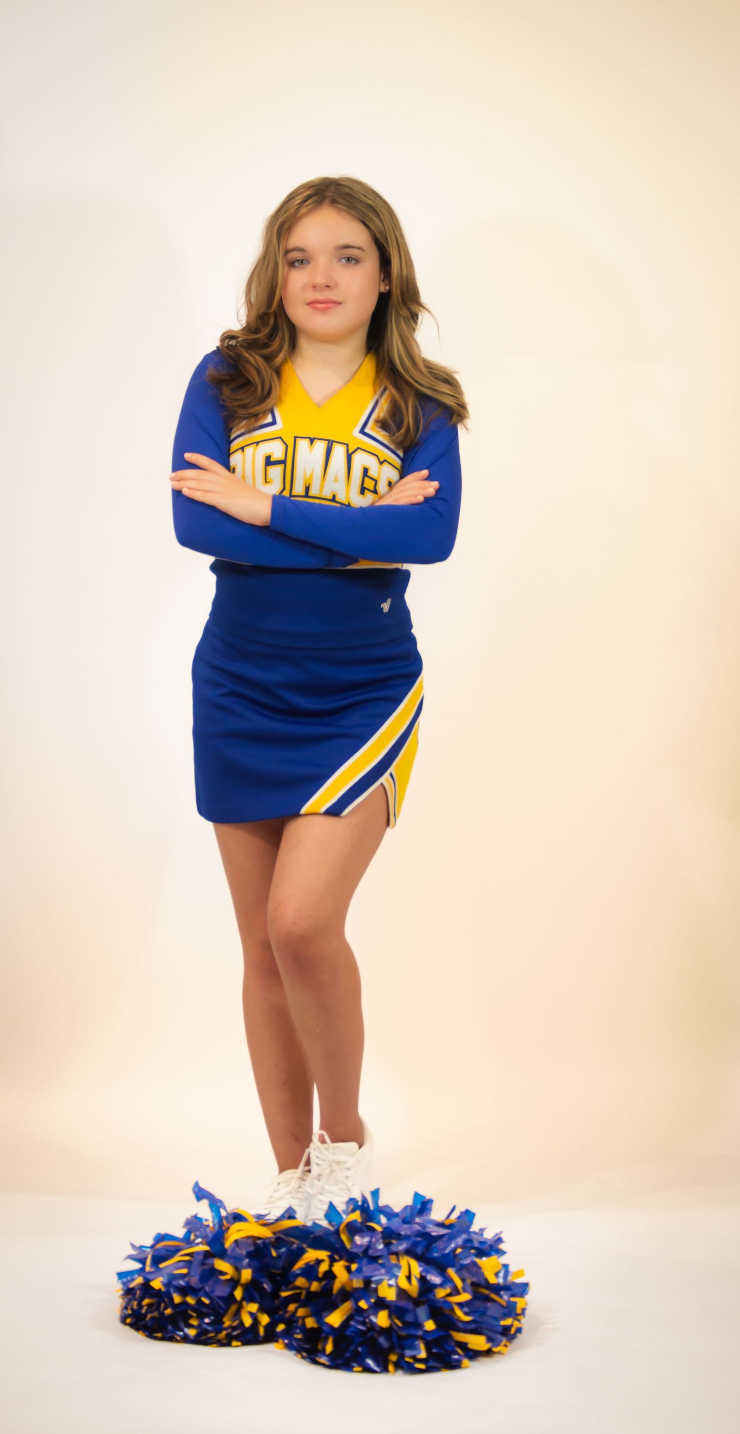 A cheerleader poses with blue and yellow pom poms in a studio setting.