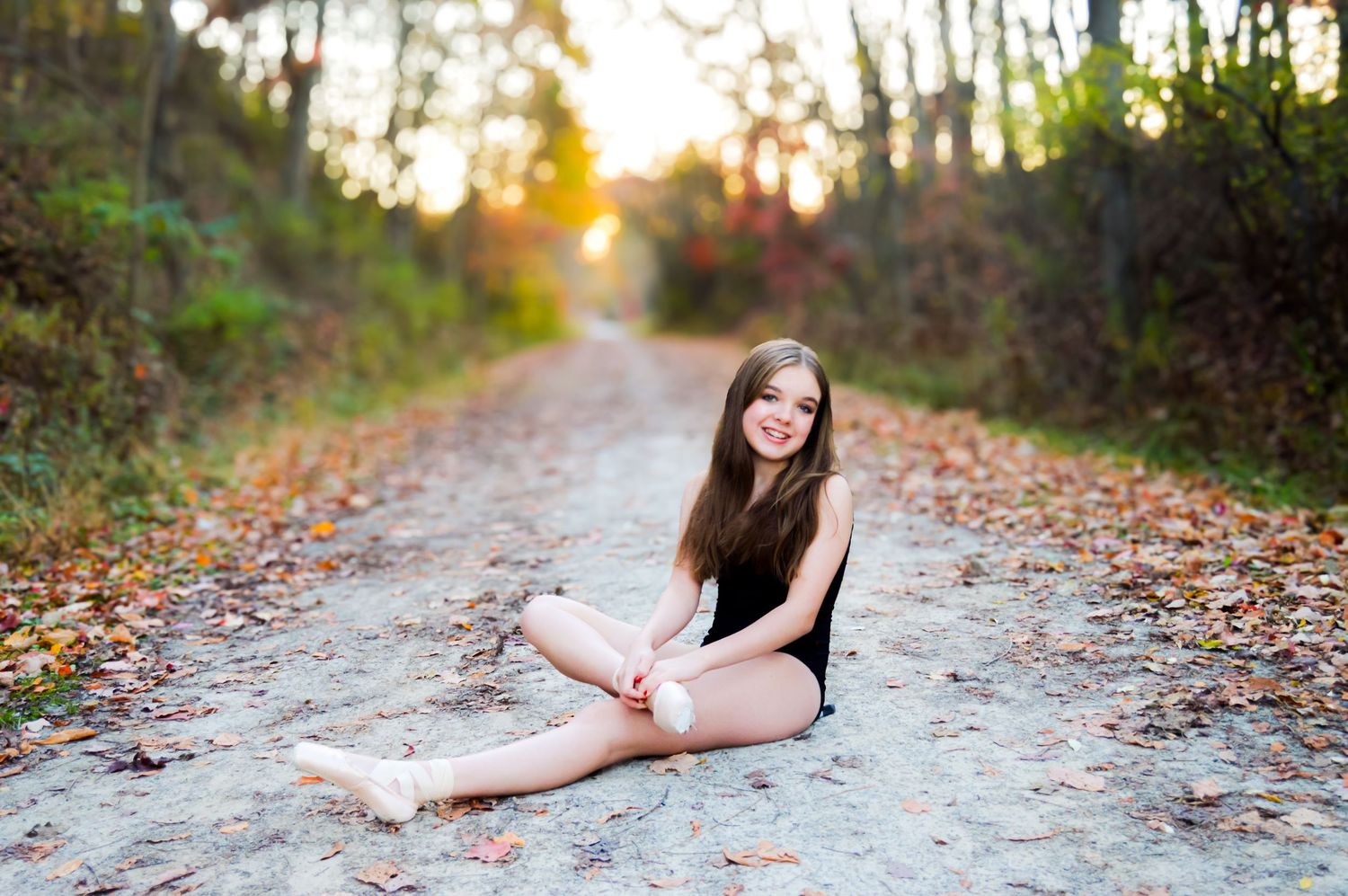 Dancer poses gracefully on leaf-covered path during autumn sunset.