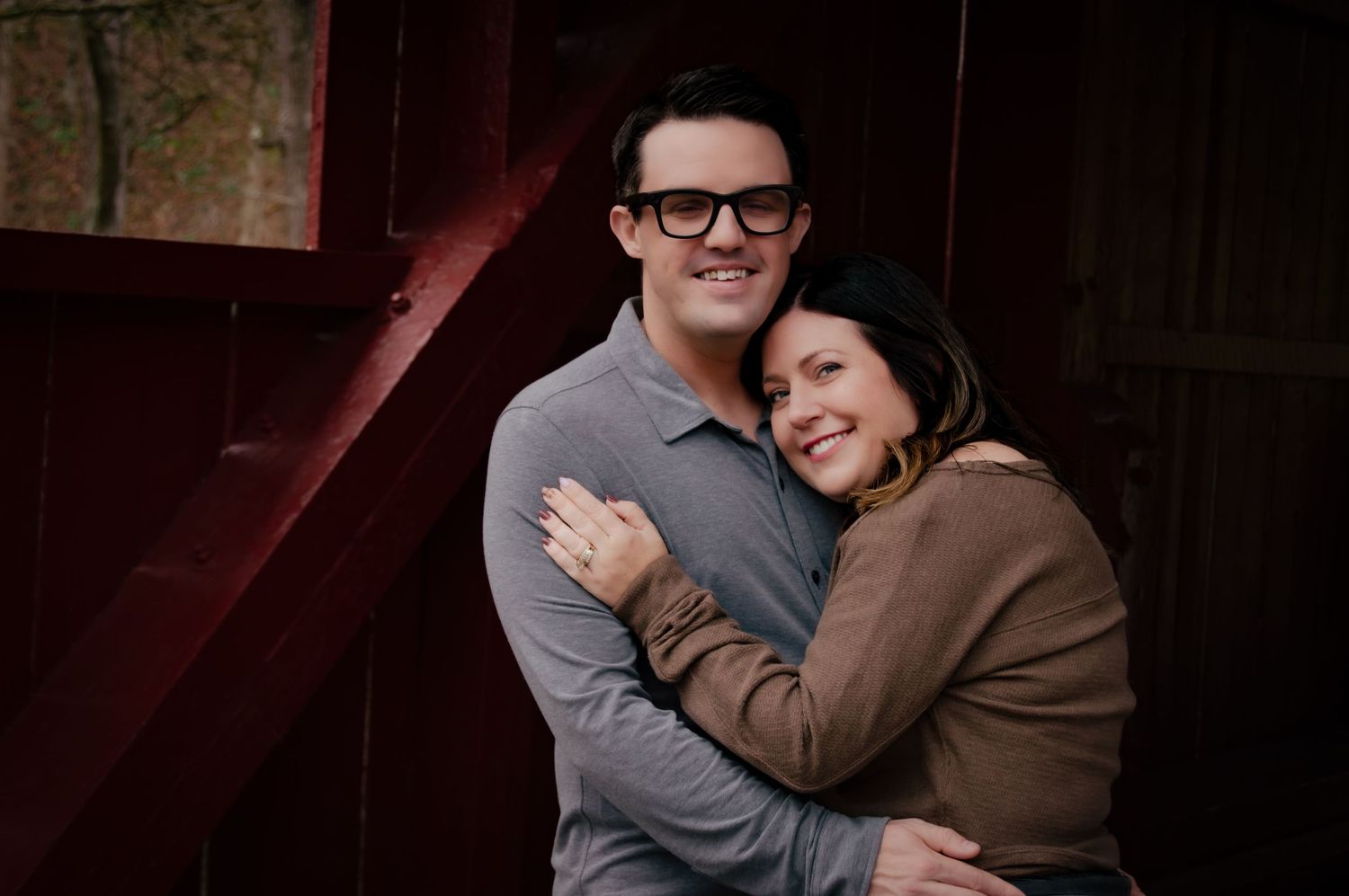 A couple embraces and smiles warmly while posing together in a dimly lit indoor setting.