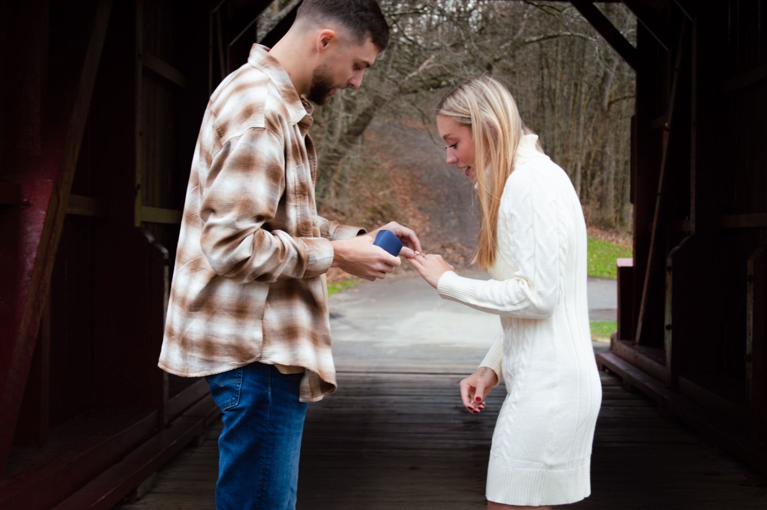 A couple shares an emotional moment during a surprise proposal at a covered bridge in the woods.