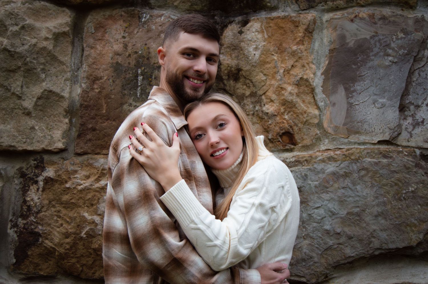A couple embraces intimately against a rustic stone wall in romantic outdoor portrait session.