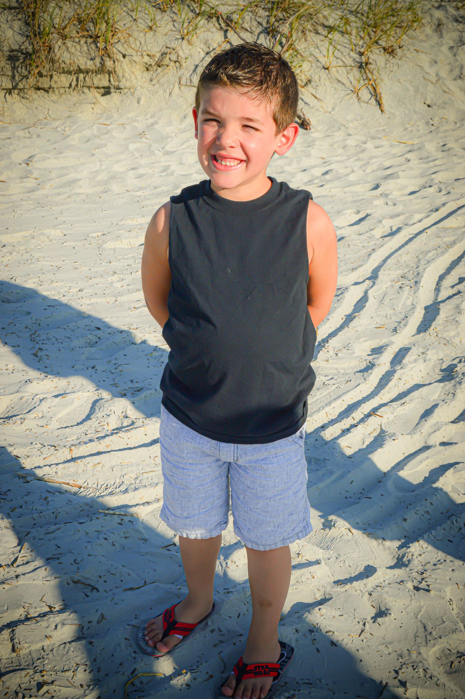 Child's shadow cast on white beach sand while walking near beach vegetation.