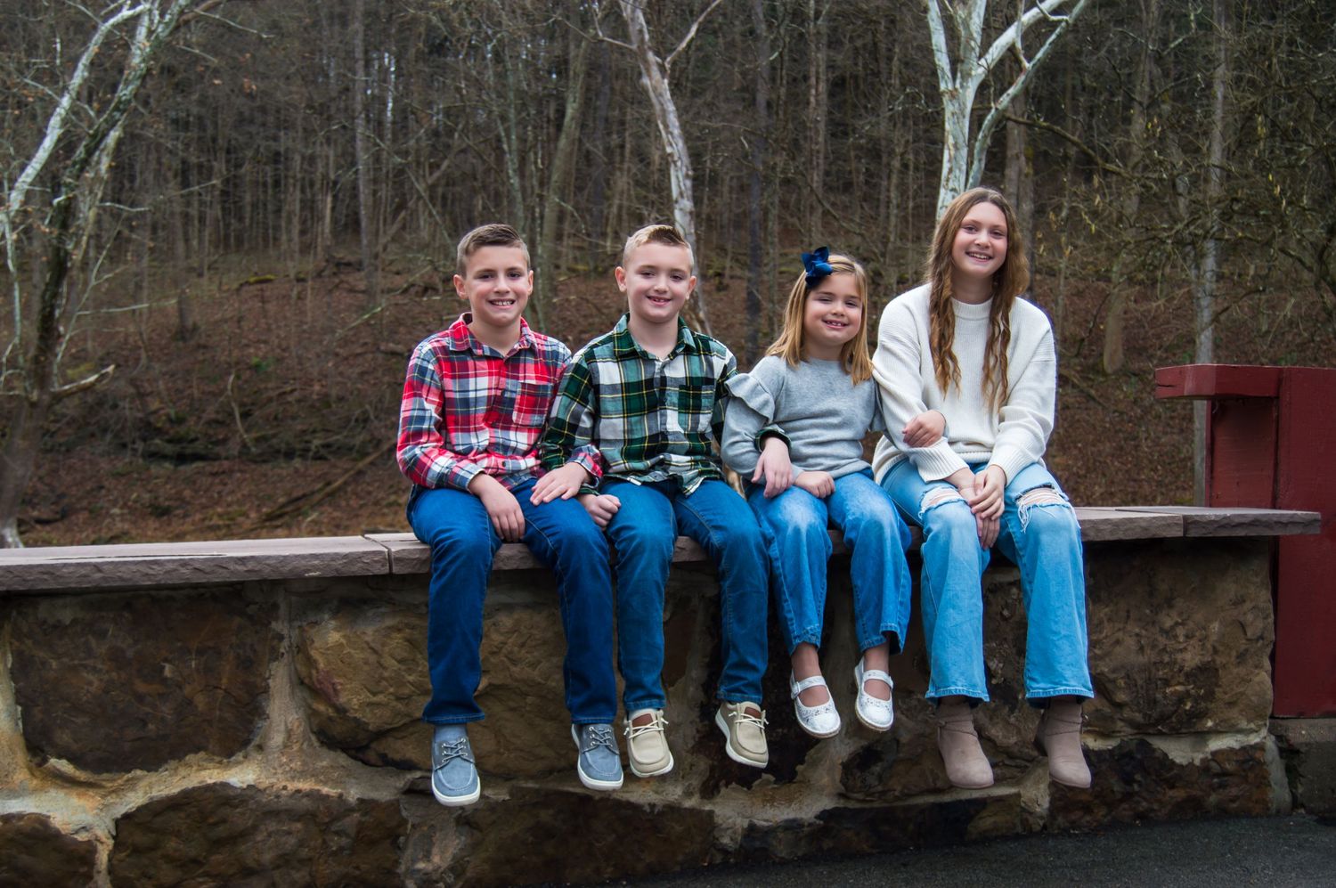 A group sits casually on wooden steps outdoors surrounded by trees in autumn weather.