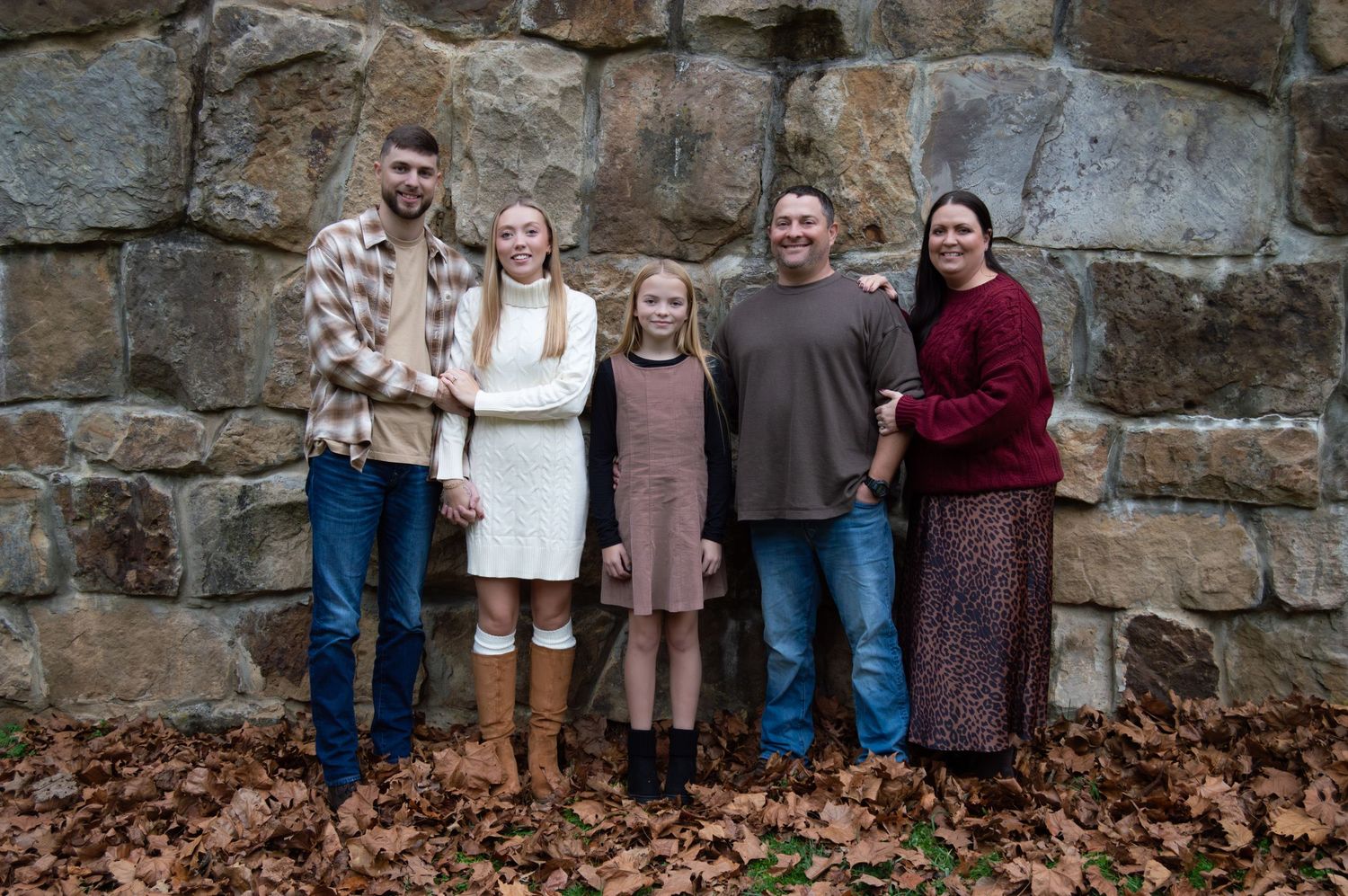Family group posing outdoors against weathered stone wall backdrop in casual attire.