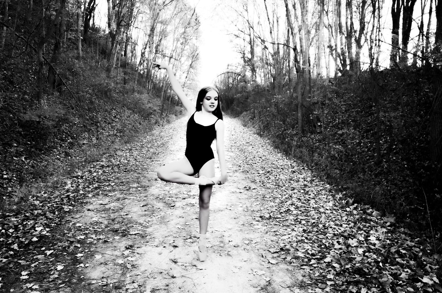 Black and white dance portraits on a wooded path covered in fallen leaves.