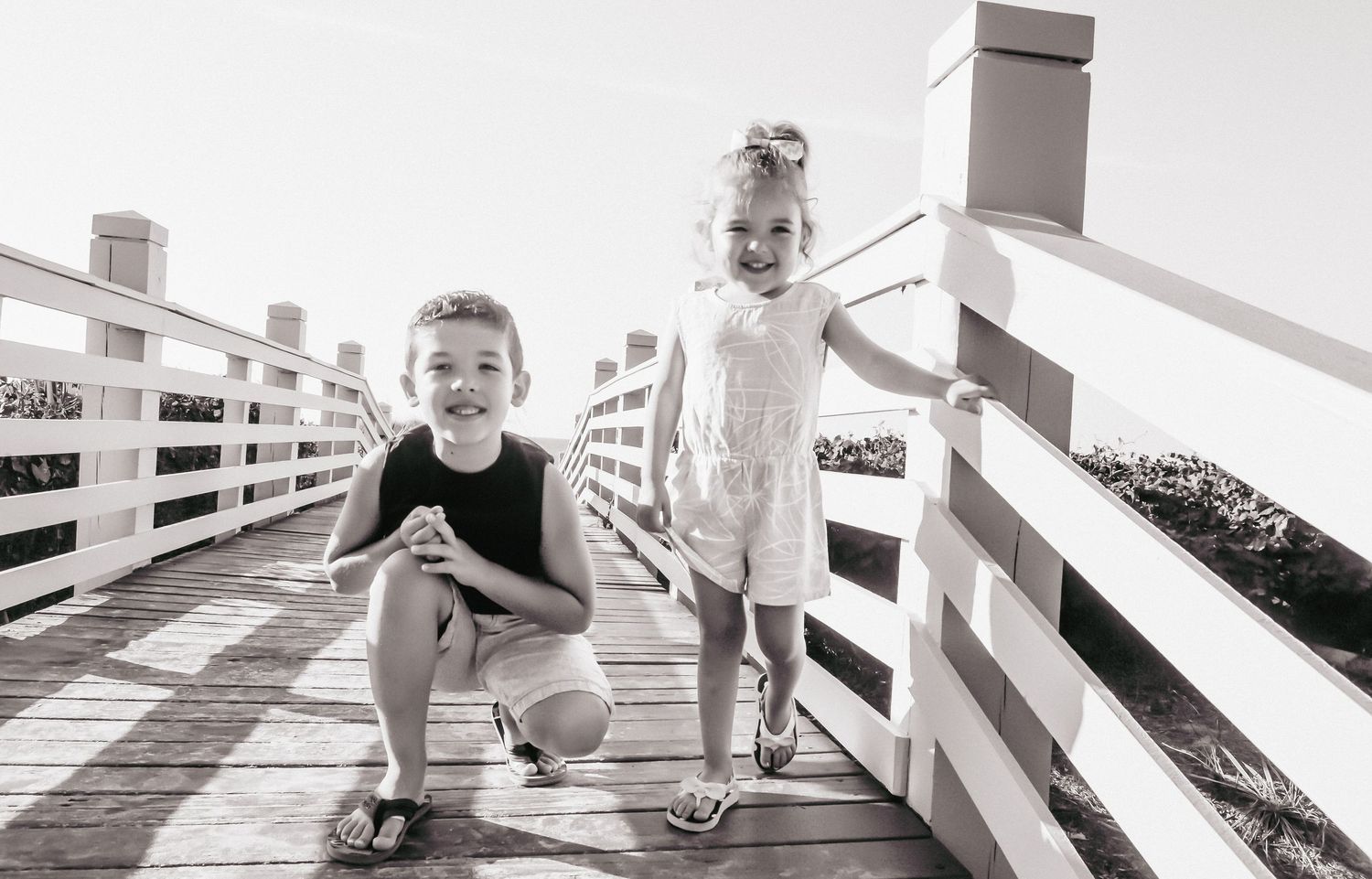 Two children pose together on a white wooden boardwalk on a sunny day.