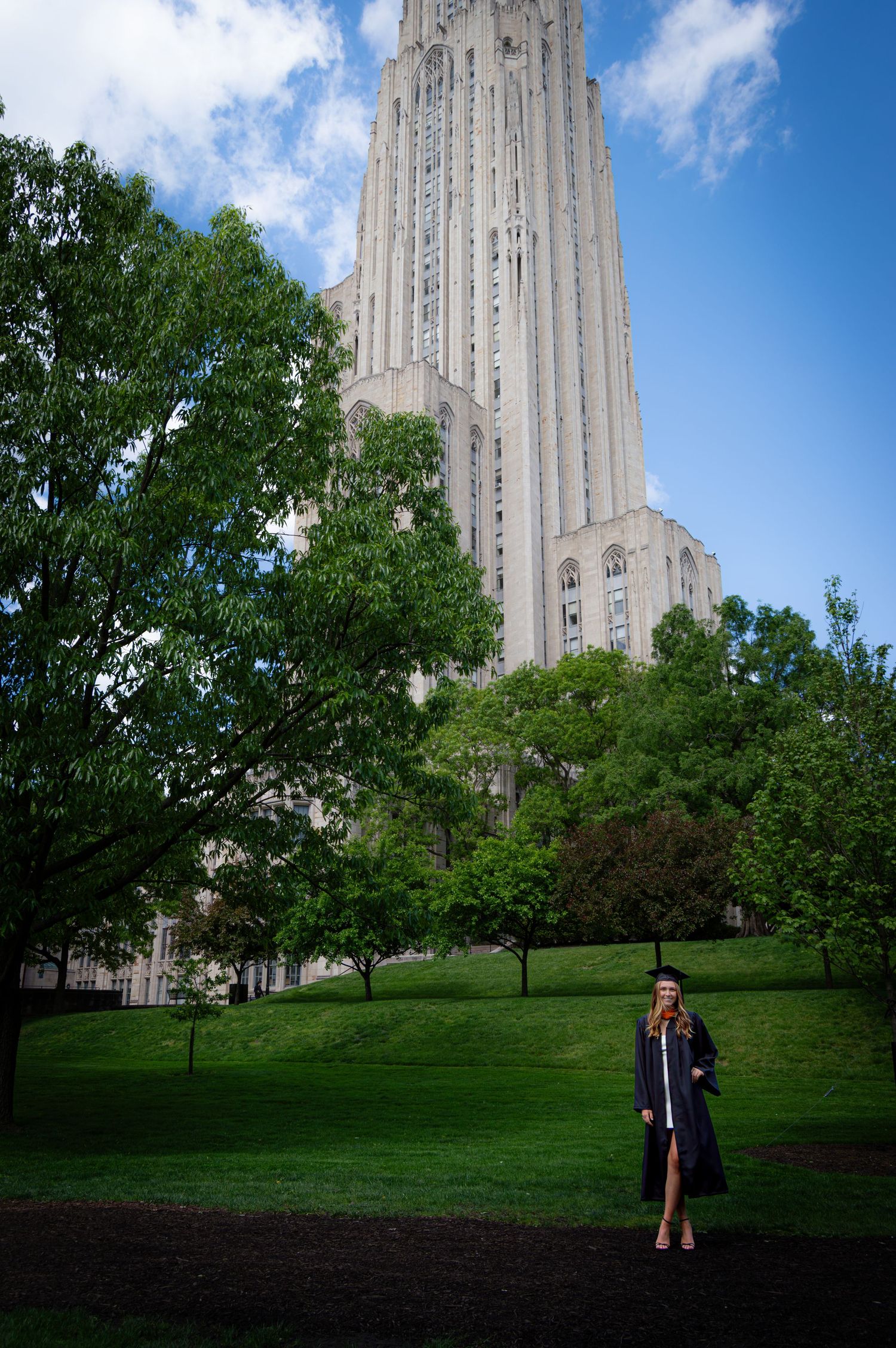 Graduate in cap and gown standing before the Cathedral of Learning at University of Pittsburgh.
