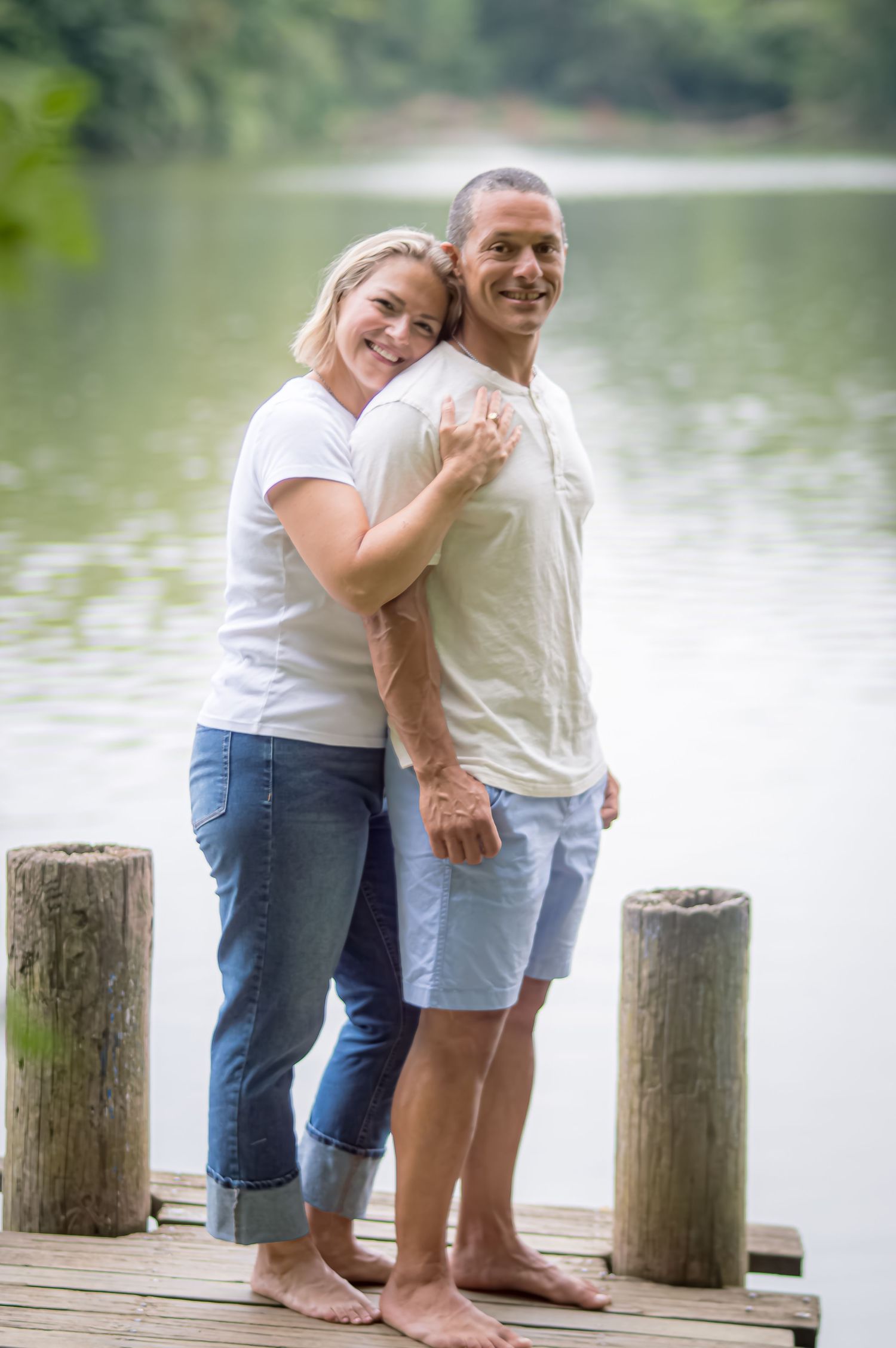 A couple shares a tender moment together while standing on a wooden dock by a serene lake.