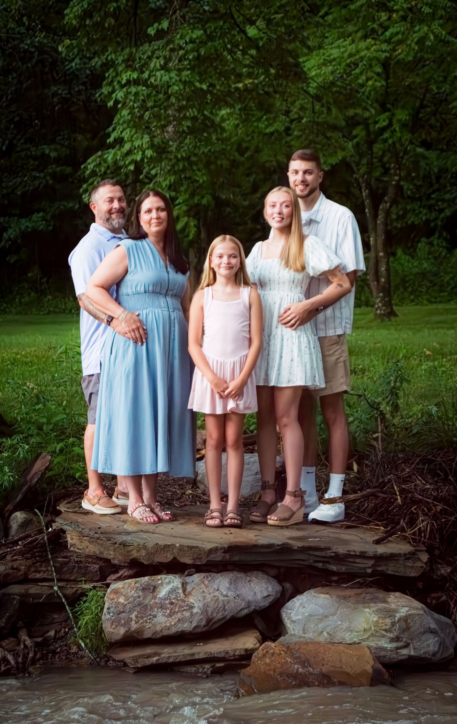 Family portrait of five people standing on stone steps in a garden setting.