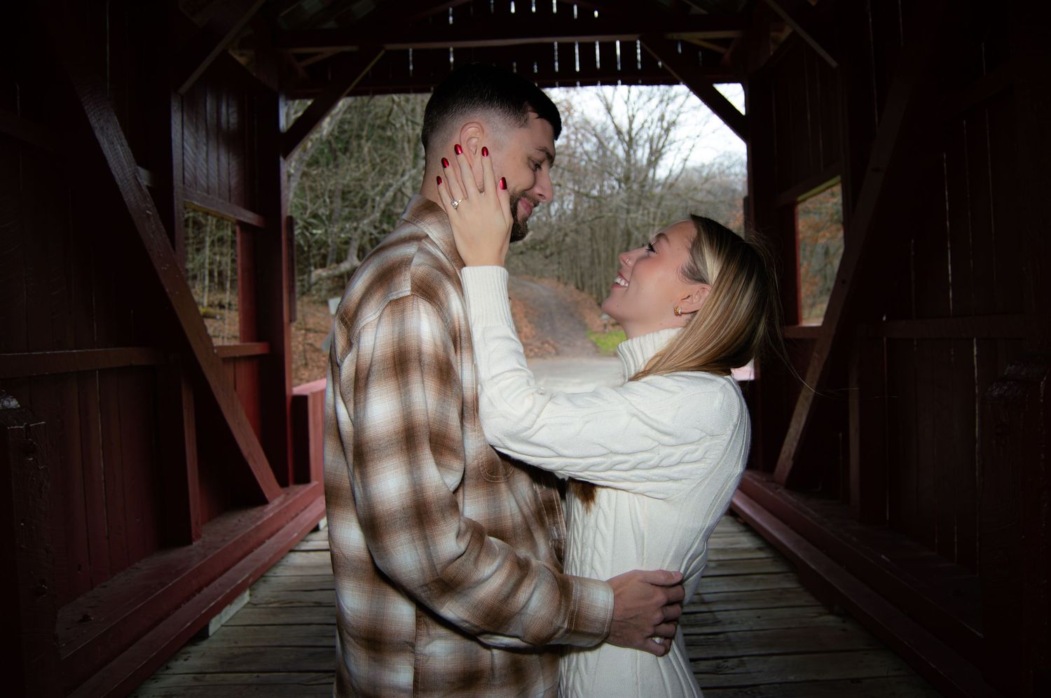 A romantic couple embraces tenderly on a covered wooden bridge during an outdoor photo session.