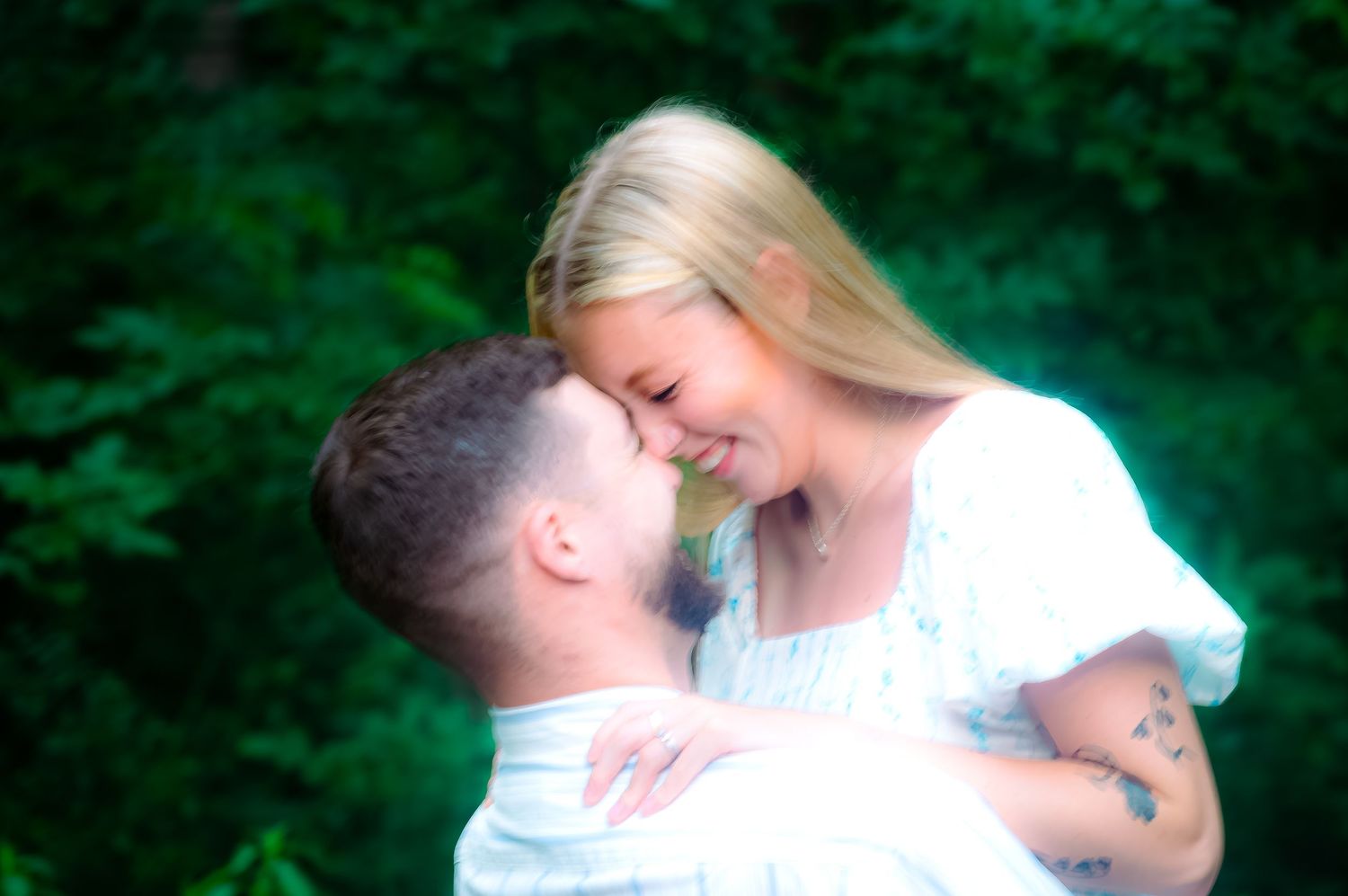 A couple sharing an intimate moment surrounded by vibrant green foliage in a natural setting.