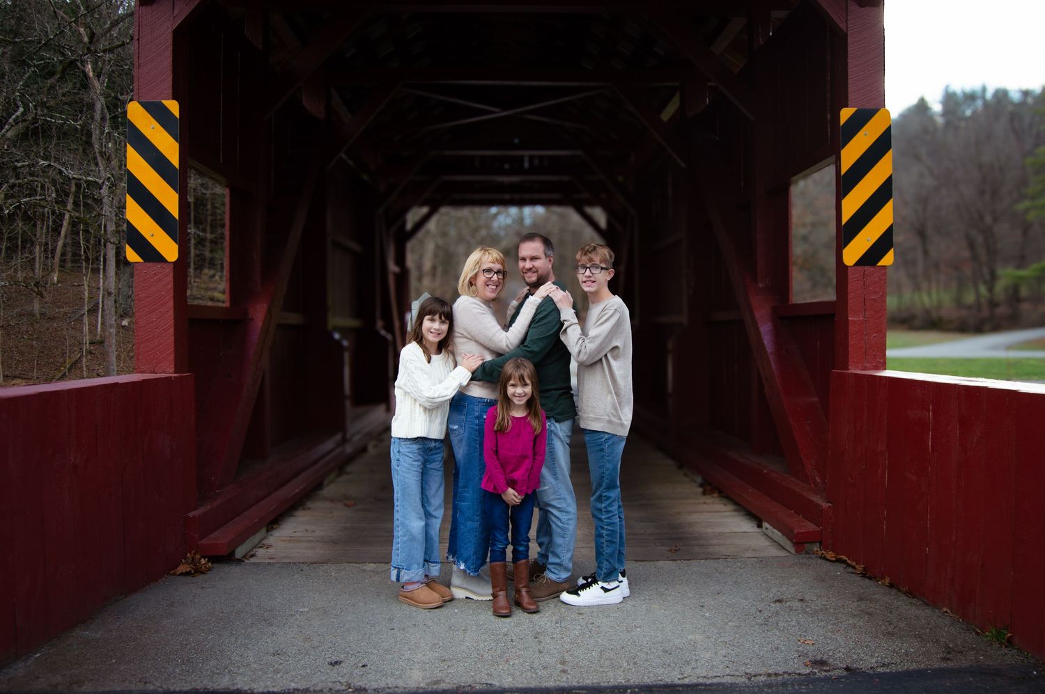 A group stands together inside a rustic red covered bridge in autumn.