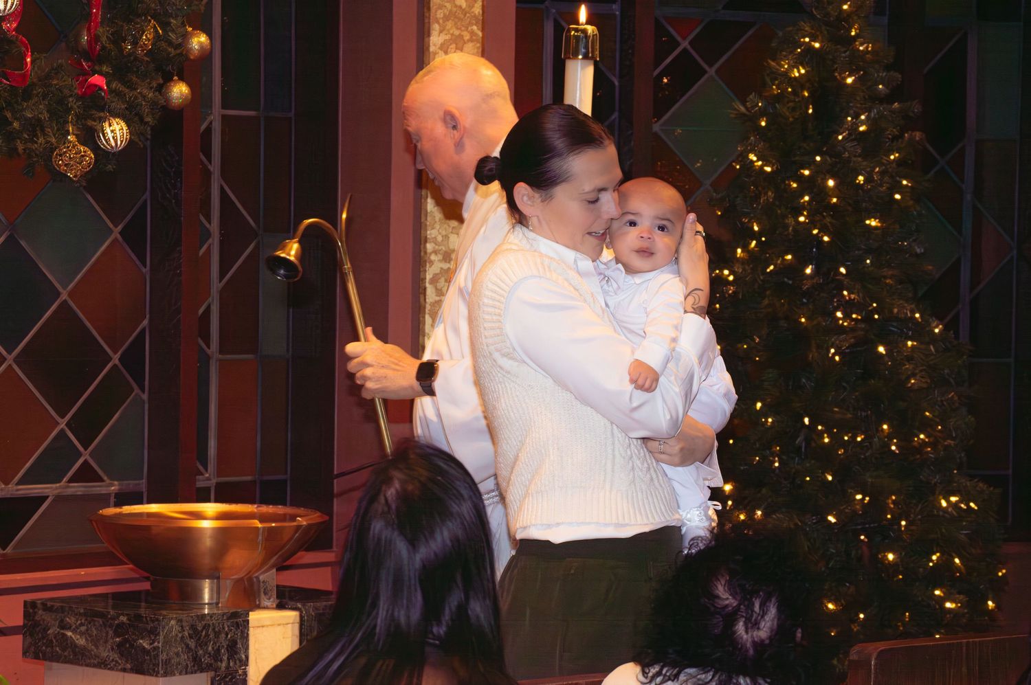 A couple dances together in front of a decorated Christmas tree at an indoor holiday celebration.