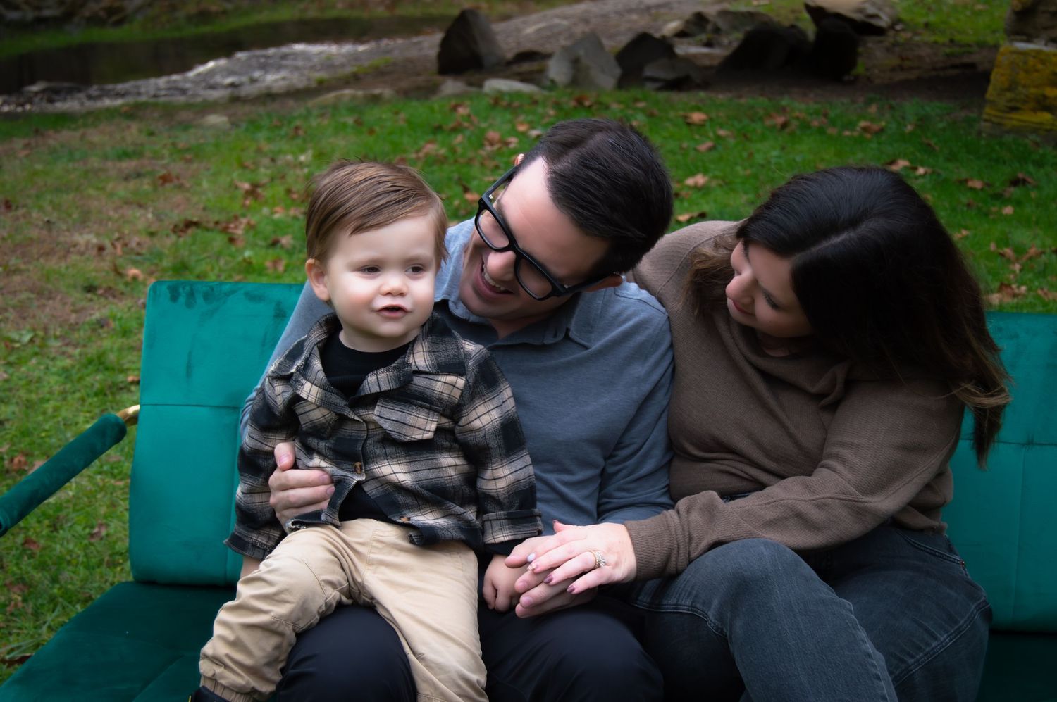 Three people sit together on a green bench outdoors enjoying a relaxed moment in nature.