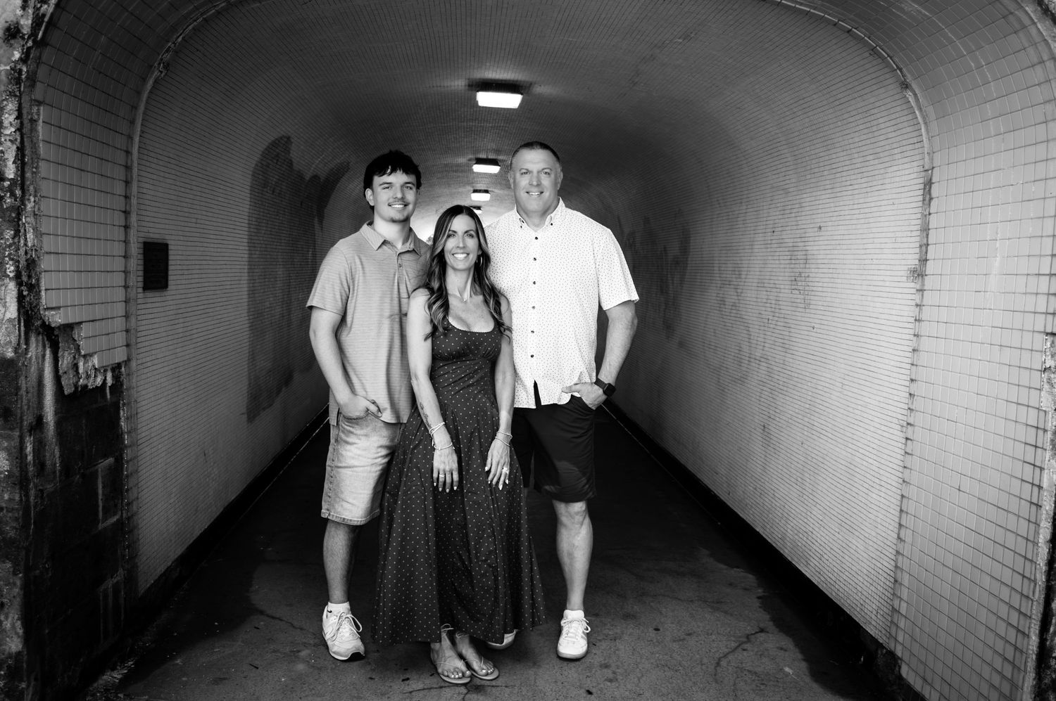 Black and white photo of three people smiling together in a tunnel hallway.