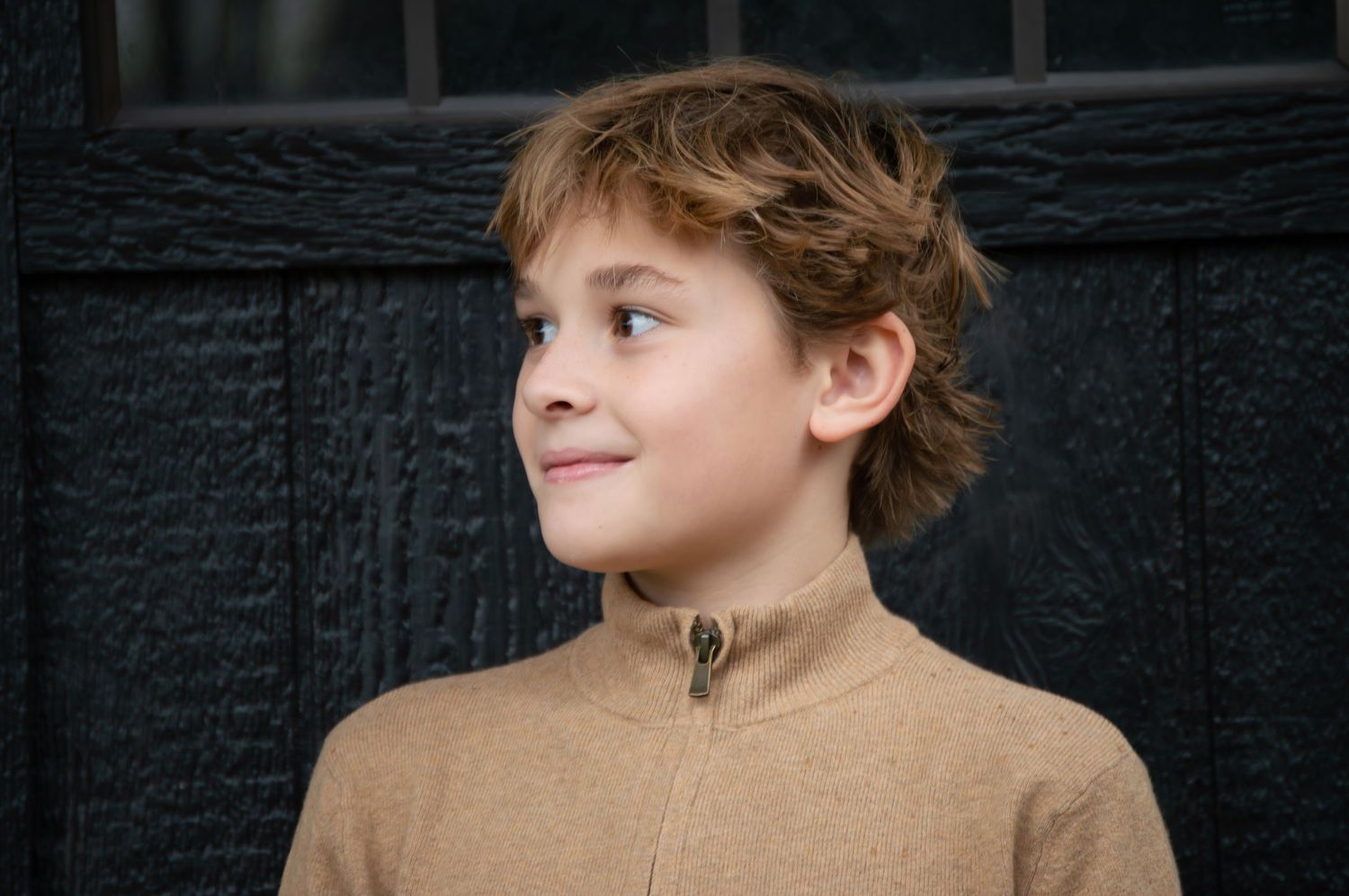 A young person with tousled hair gazes upward with a contemplative expression against a dark background.