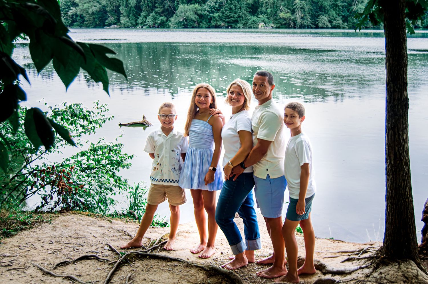 Family enjoying a summer day together by a serene lake surrounded by trees and nature.