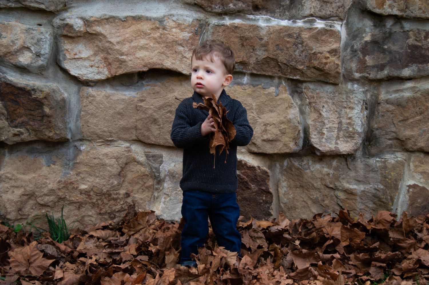 A young child plays and laughs while exploring a rocky outdoor area with stone walls.