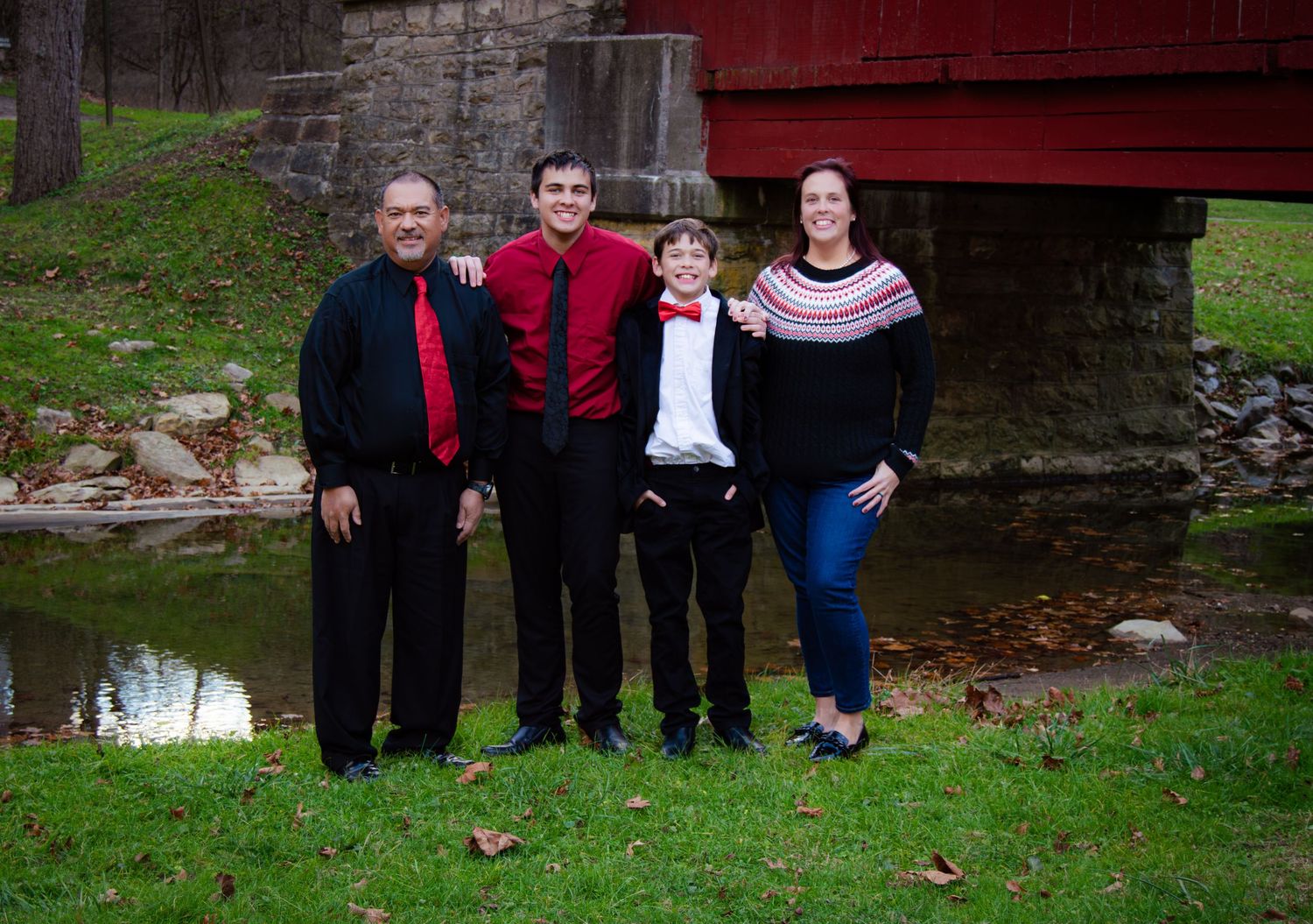 Family gathering outdoors near stone wall and red barn on grassy lawn.