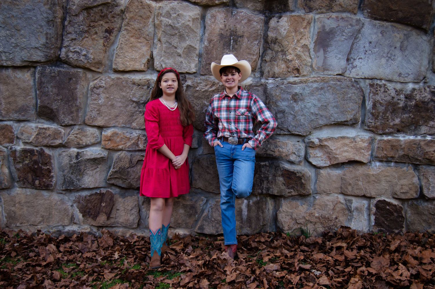 A couple stands against a rustic stone wall during an autumn engagement photo session.