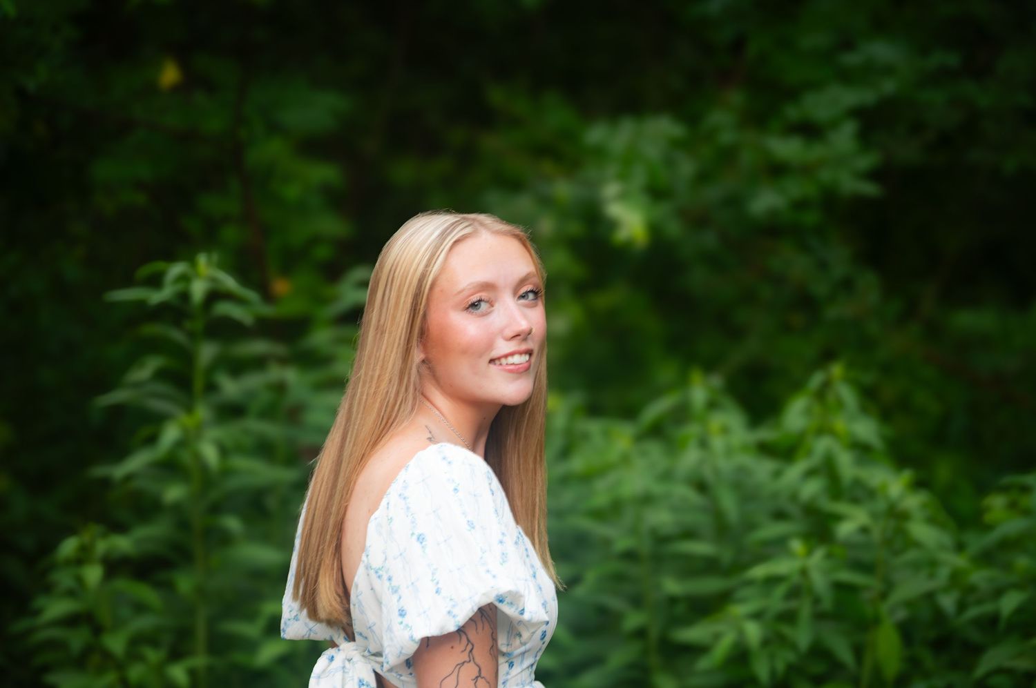 Portrait of someone in a white dress smiling against a green garden background.
