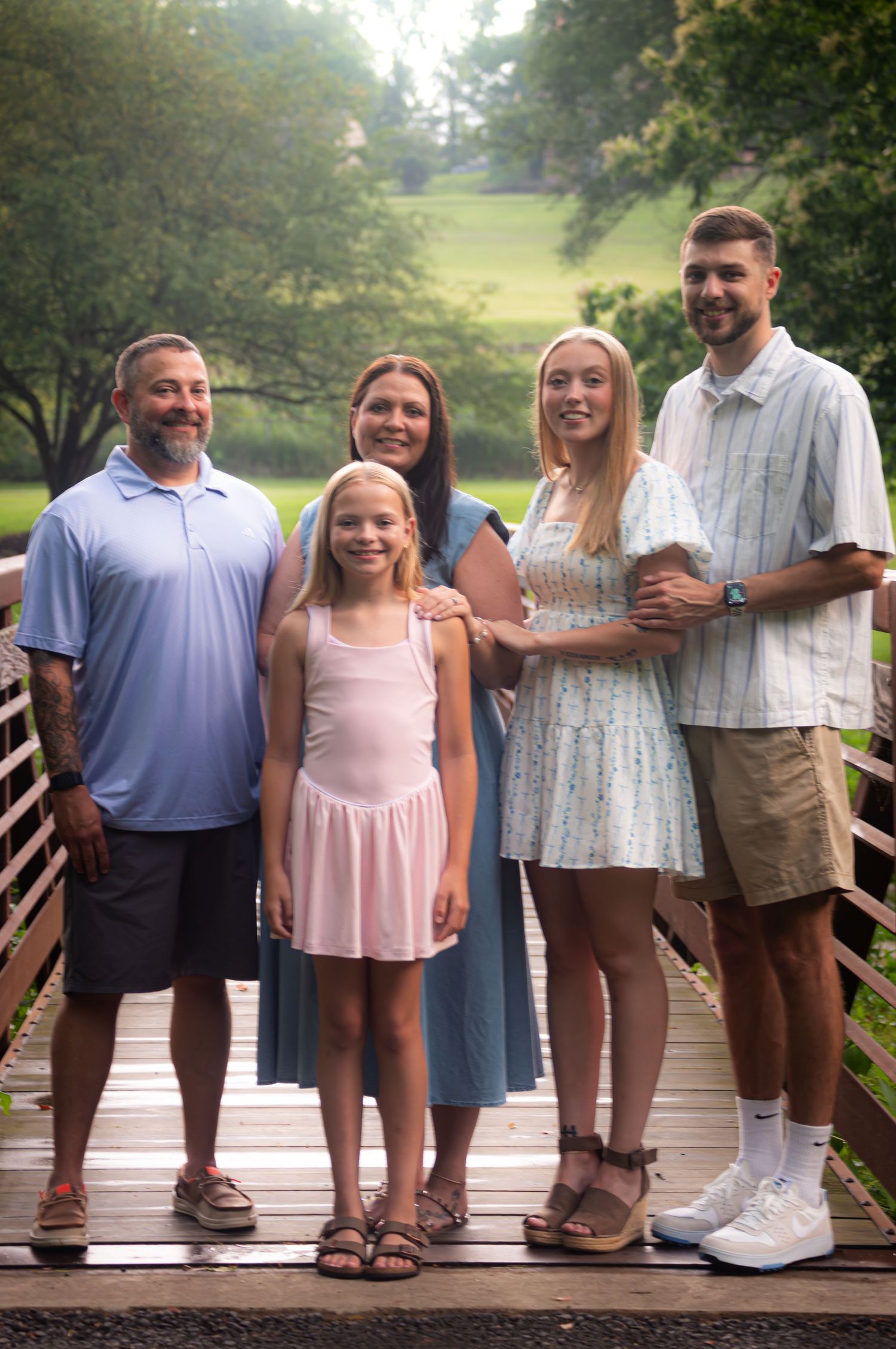 Family of five standing together on a wooden bridge in a park setting.