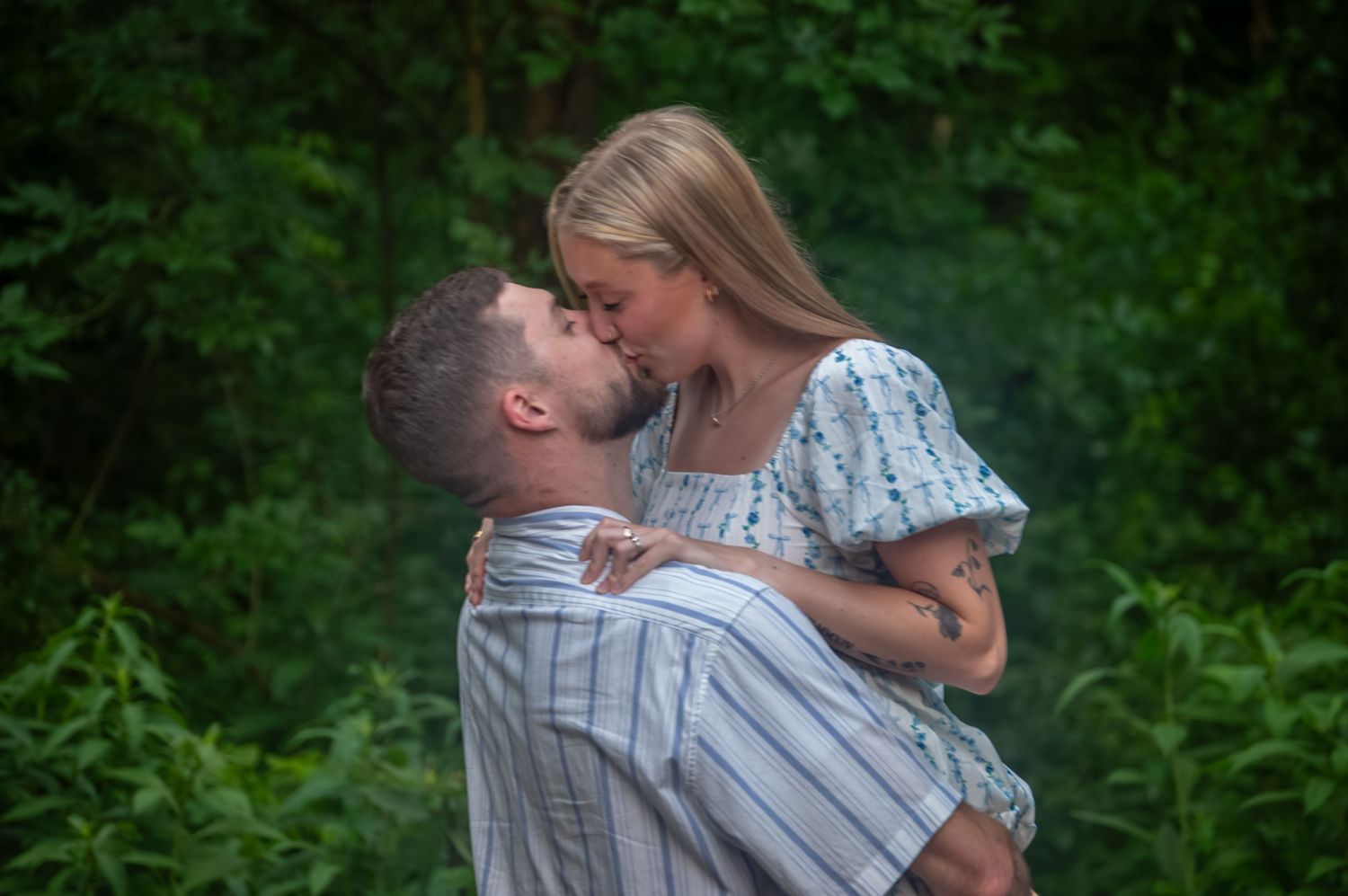 Romantic couple embraces in a lush green garden setting during an engagement photo session.