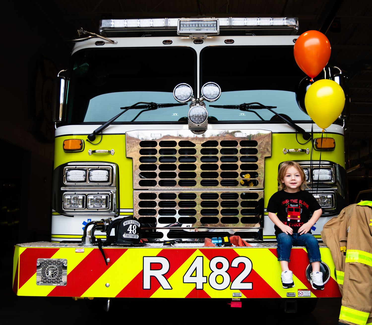 Emergency vehicles with bright yellow and red reflective stripes line up in a row at a safety demonstration event.