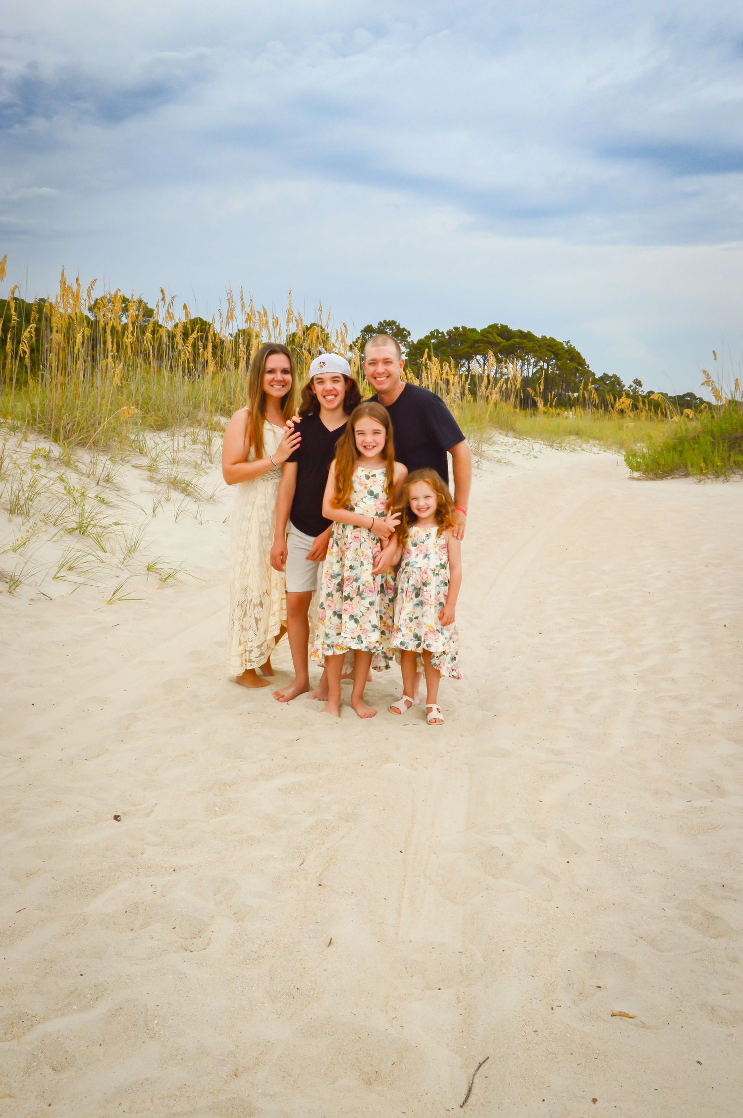 A family group stands together on white sand dunes with tall grass and blue sky in the background.
