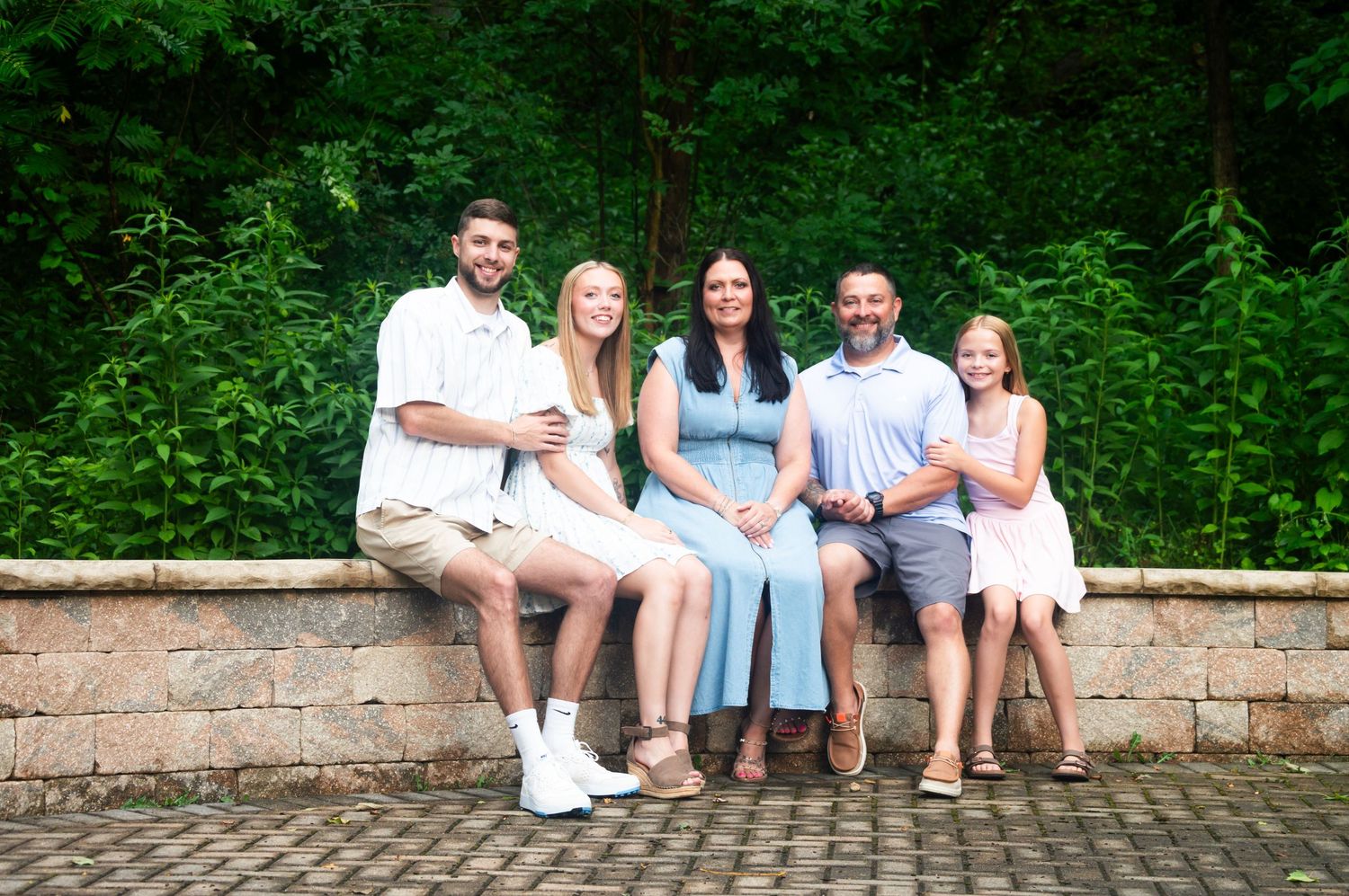 Family portrait session in a lush green garden setting with coordinated casual outfits.