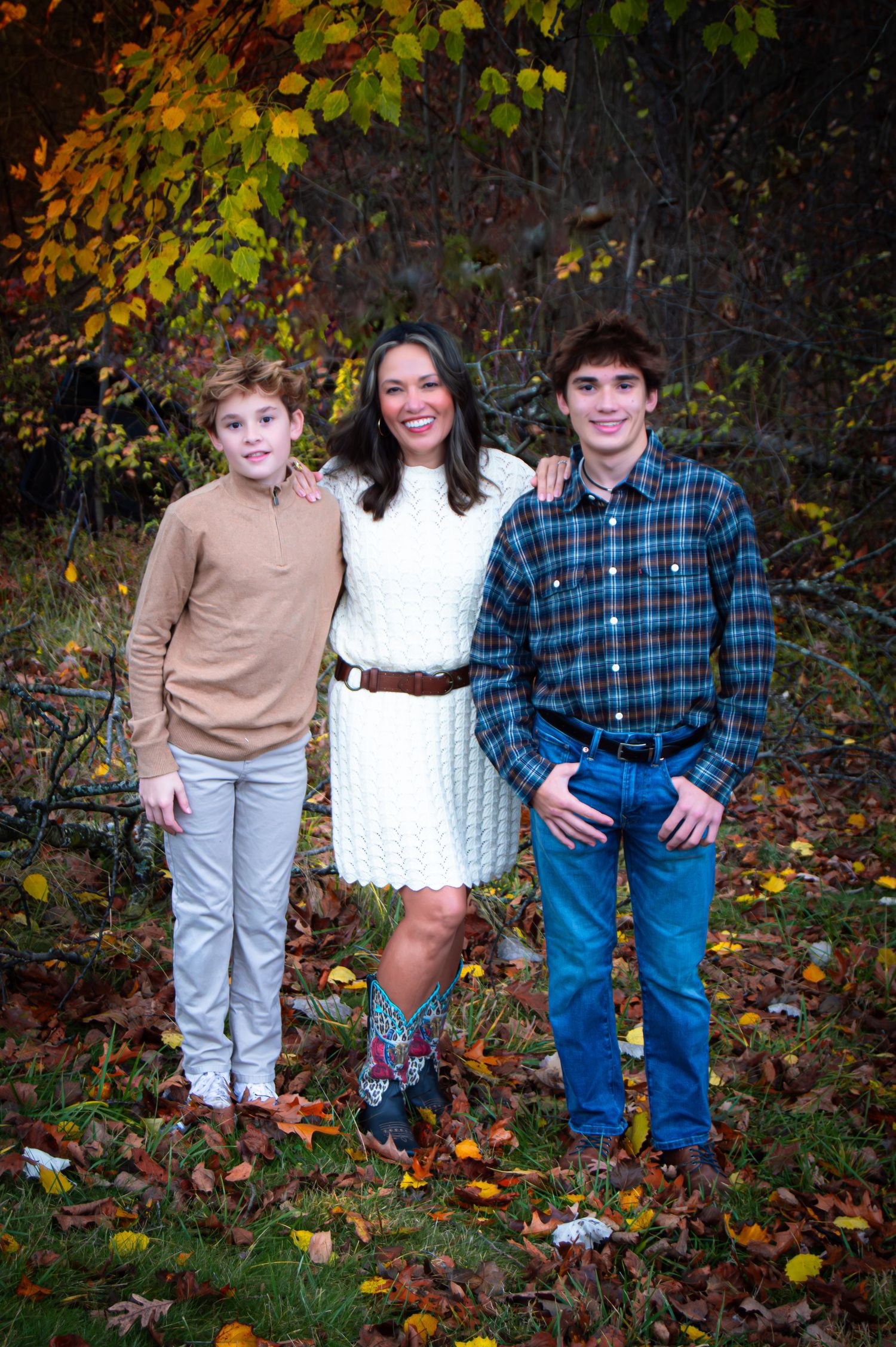Three people stand together among fallen autumn leaves and colorful trees.
