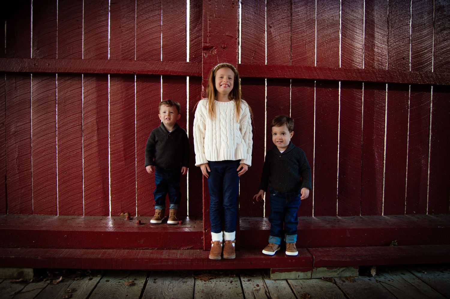 Five figures peek through slats of a dark red wooden fence creating a playful and mysterious atmosphere.