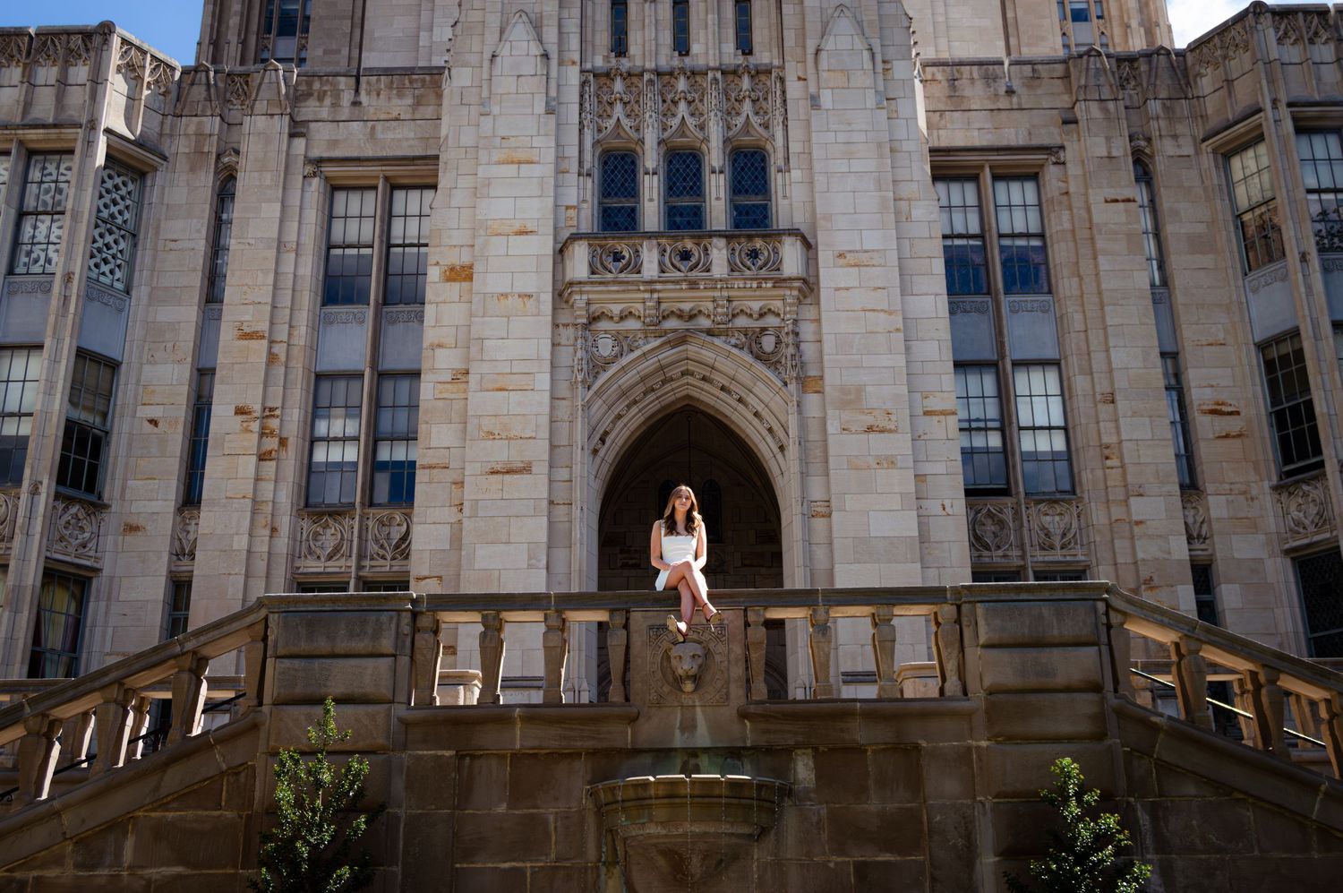 Woman sitting on stone steps outside grand Gothic university building facade.