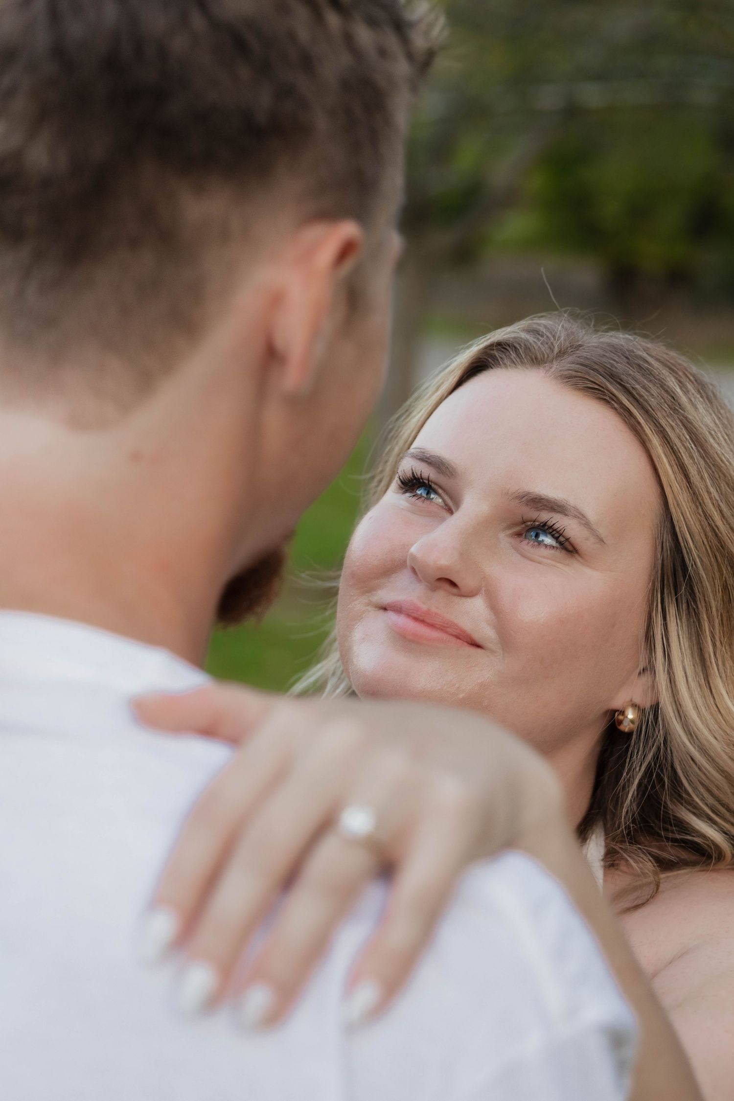 Smiling blonde woman with blue eyes gazing lovingly at her partner, wearing an engagement ring.