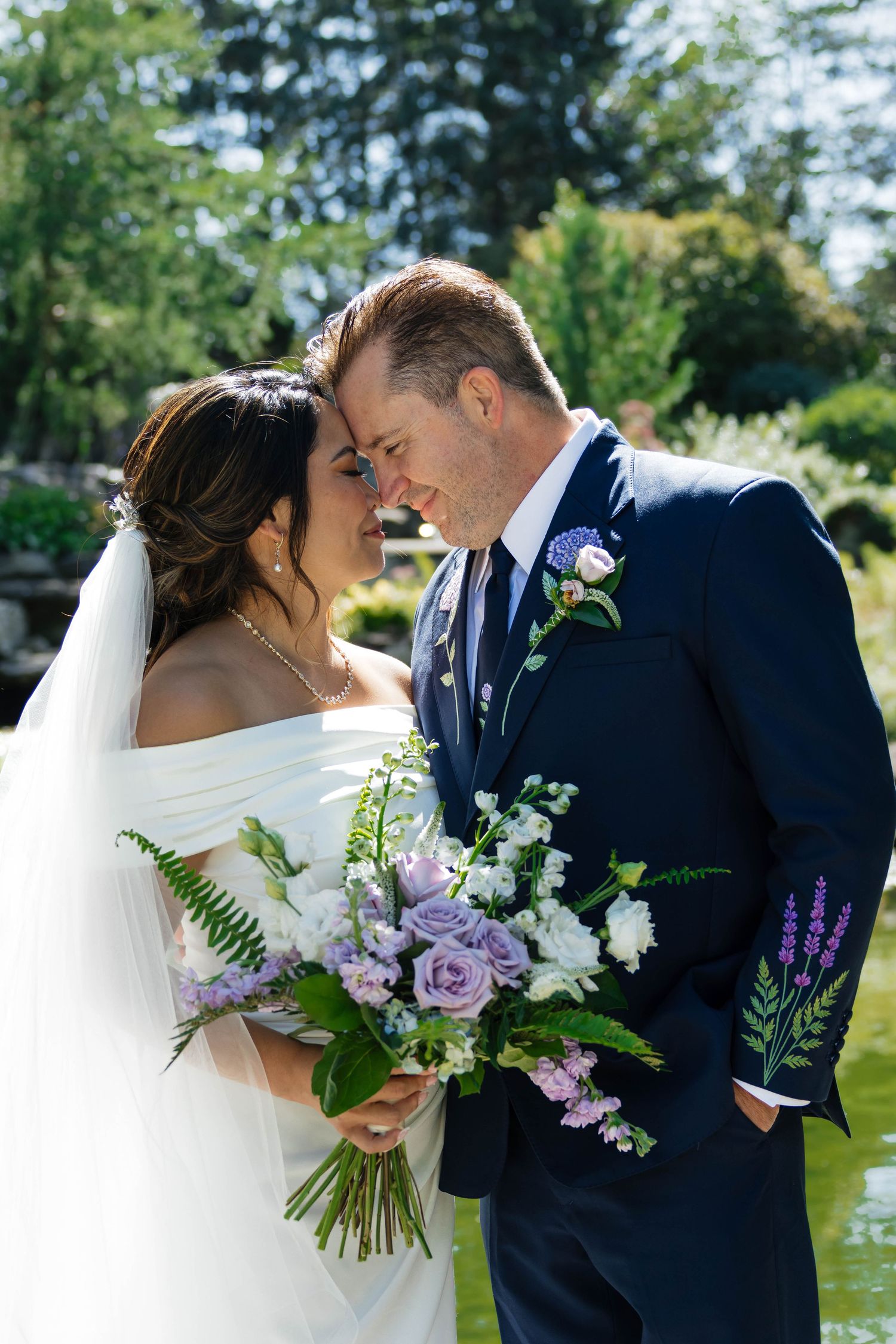 Bride and groom sharing an intimate forehead touch while holding a lavender and white bouquet.