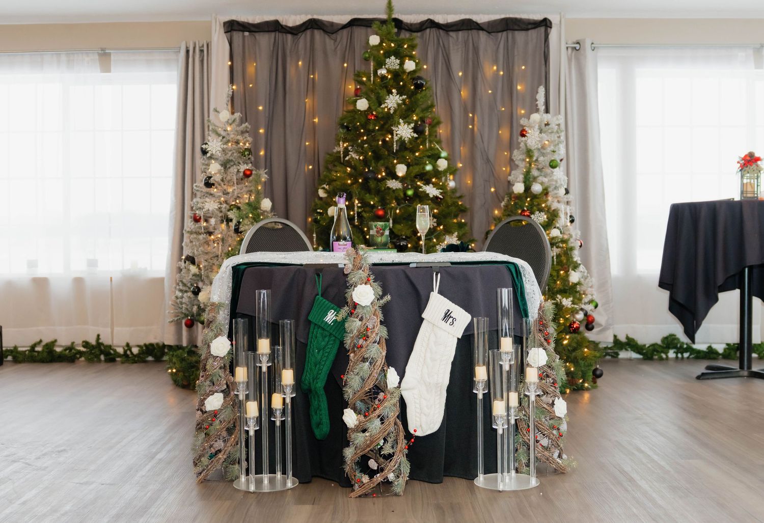 Elegant Christmas wedding reception sweetheart table decorated with holiday trees, stockings, and candles.