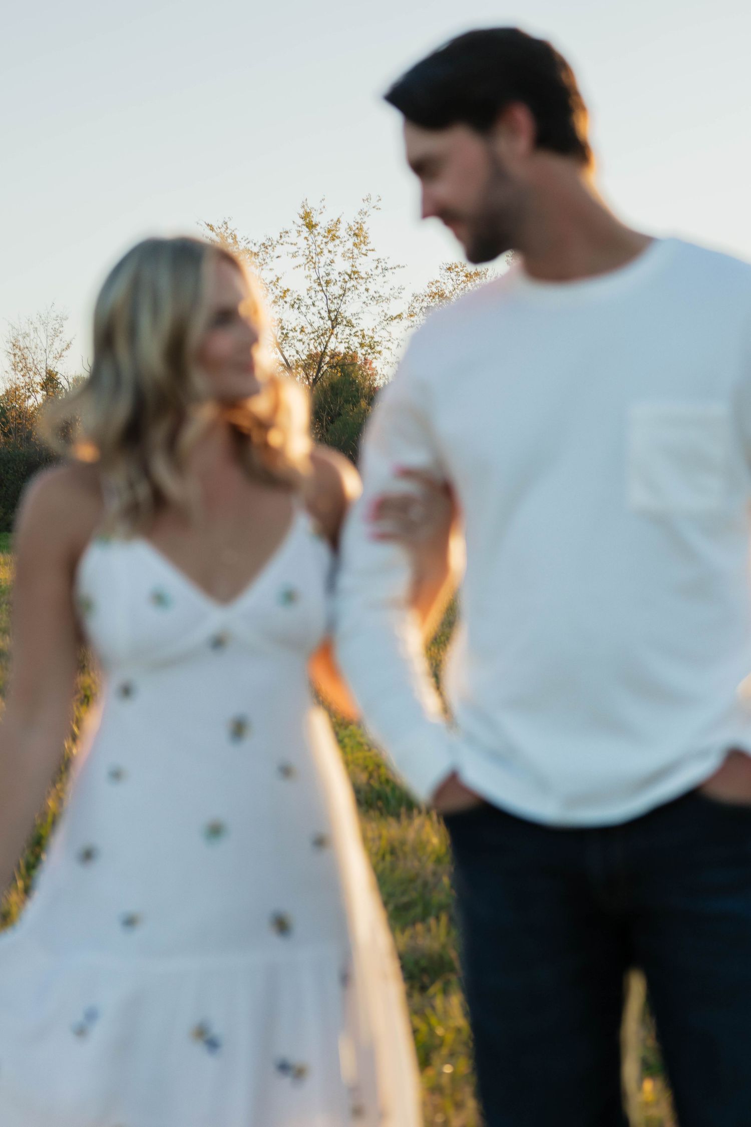 Blurred romantic couple walking together in a field during a warm sunset evening.