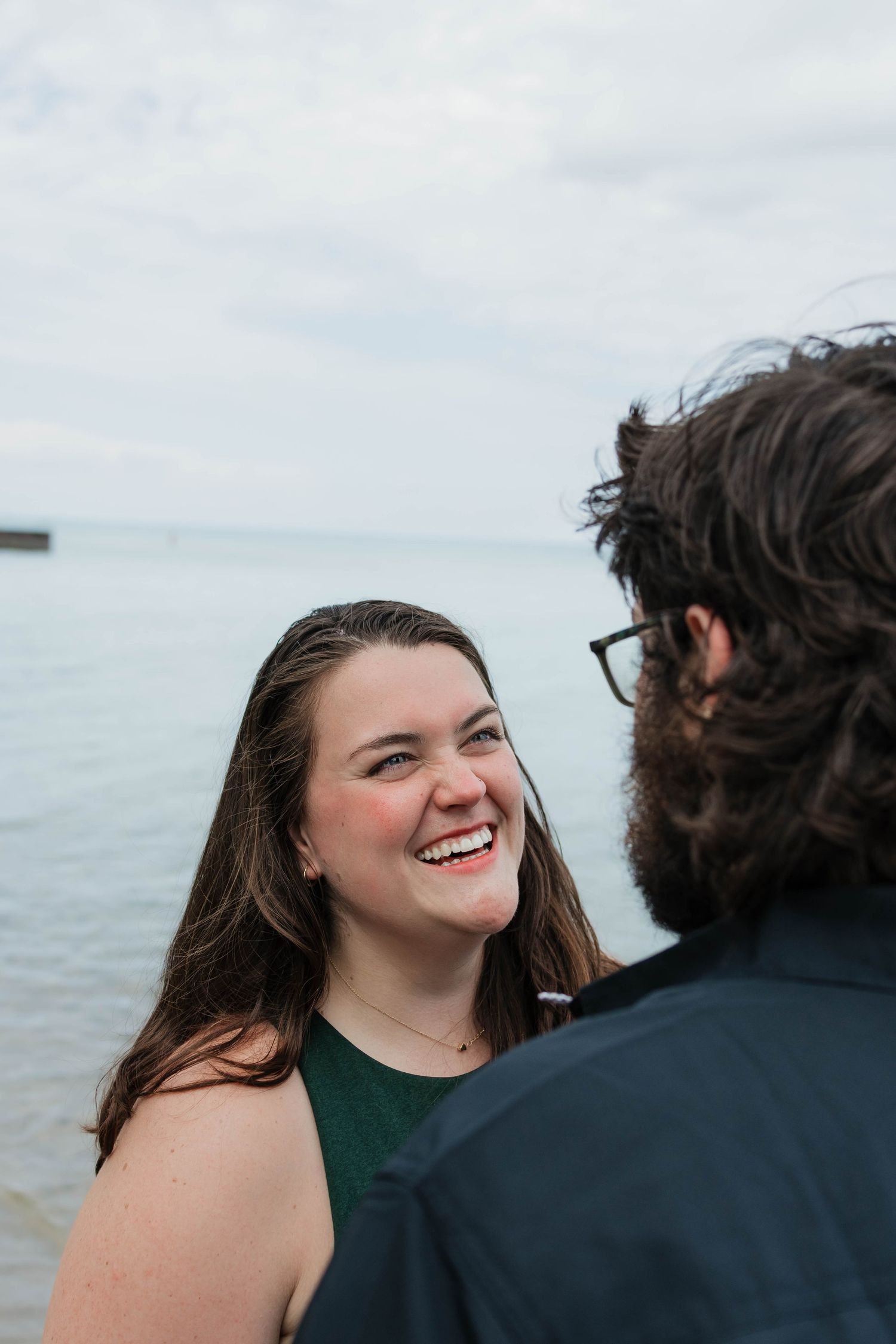 A smiling woman gazes happily at her partner with a serene ocean backdrop behind them.