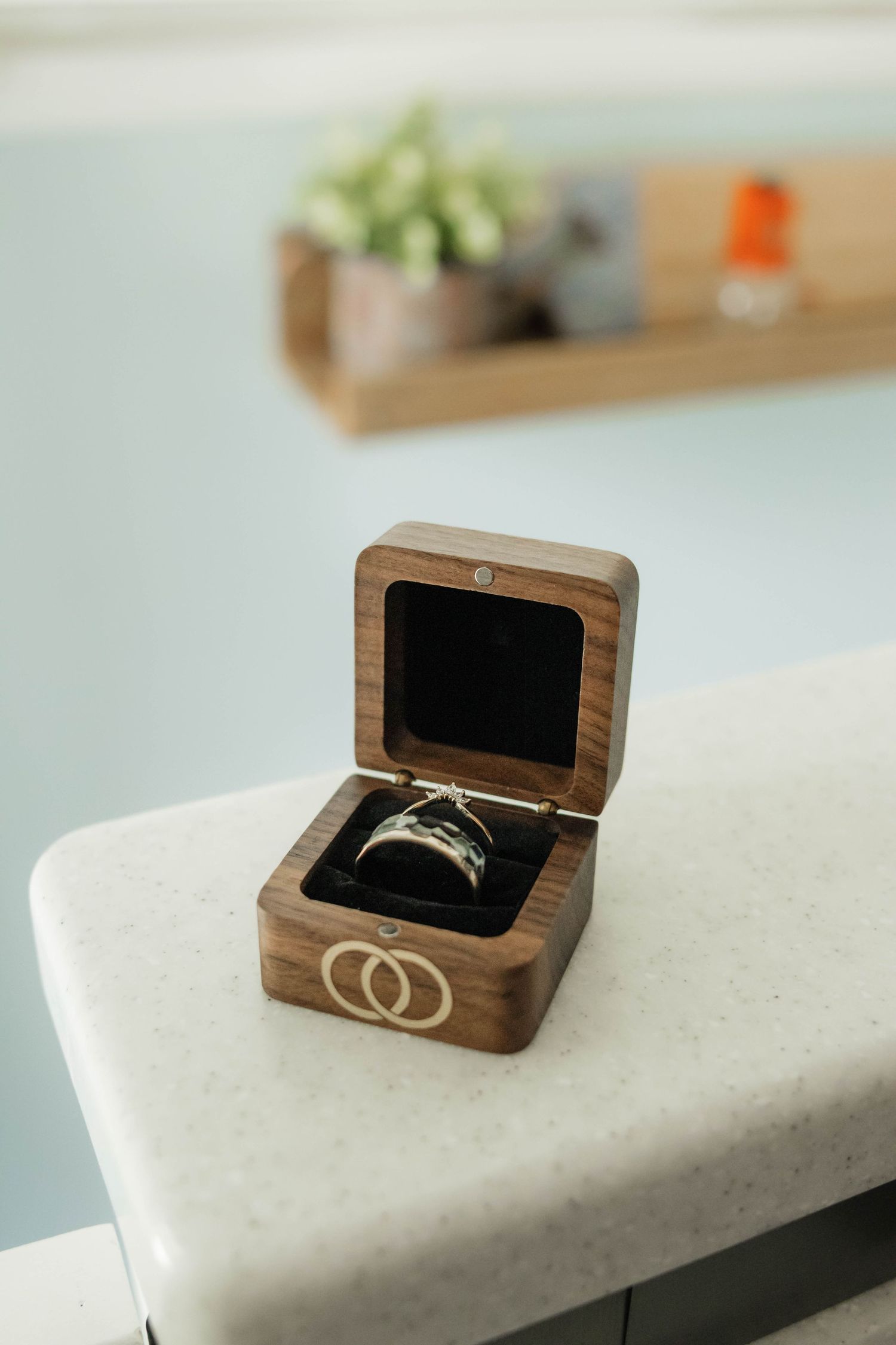 Wedding rings displayed in an elegant wooden ring box with engraved interlocking circles on white marble surface.