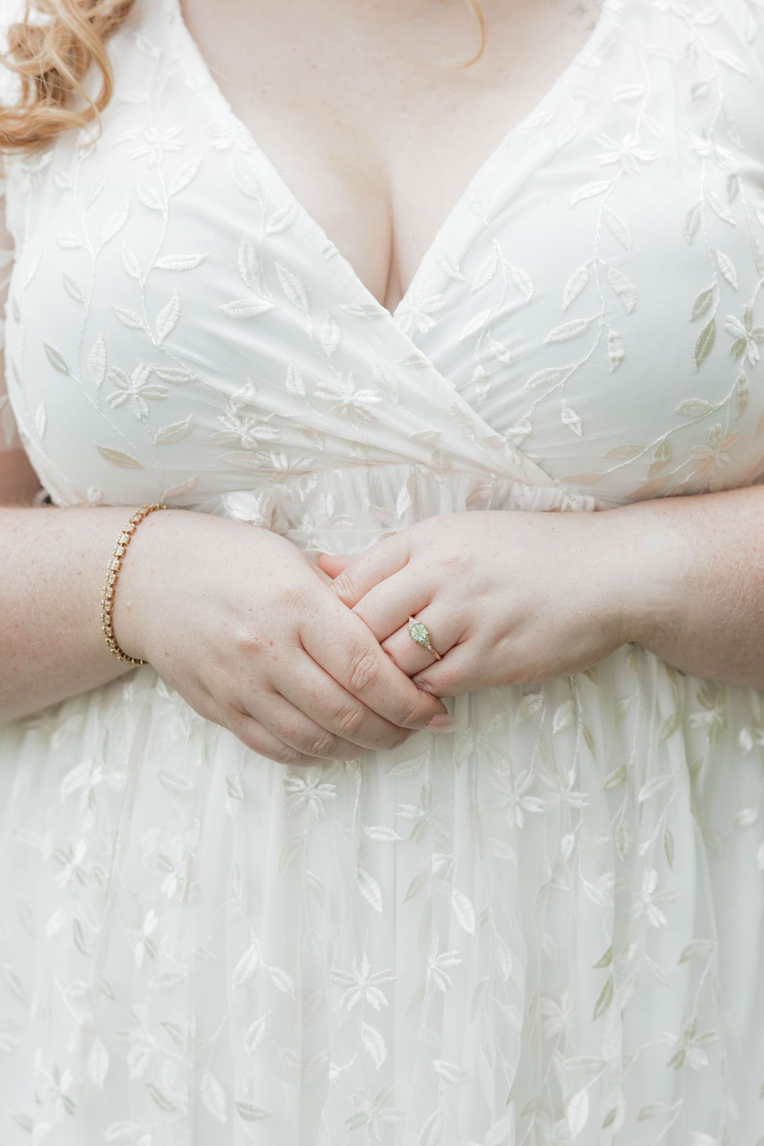Close-up of bride in white lace wedding gown with gold bracelet and engagement ring.