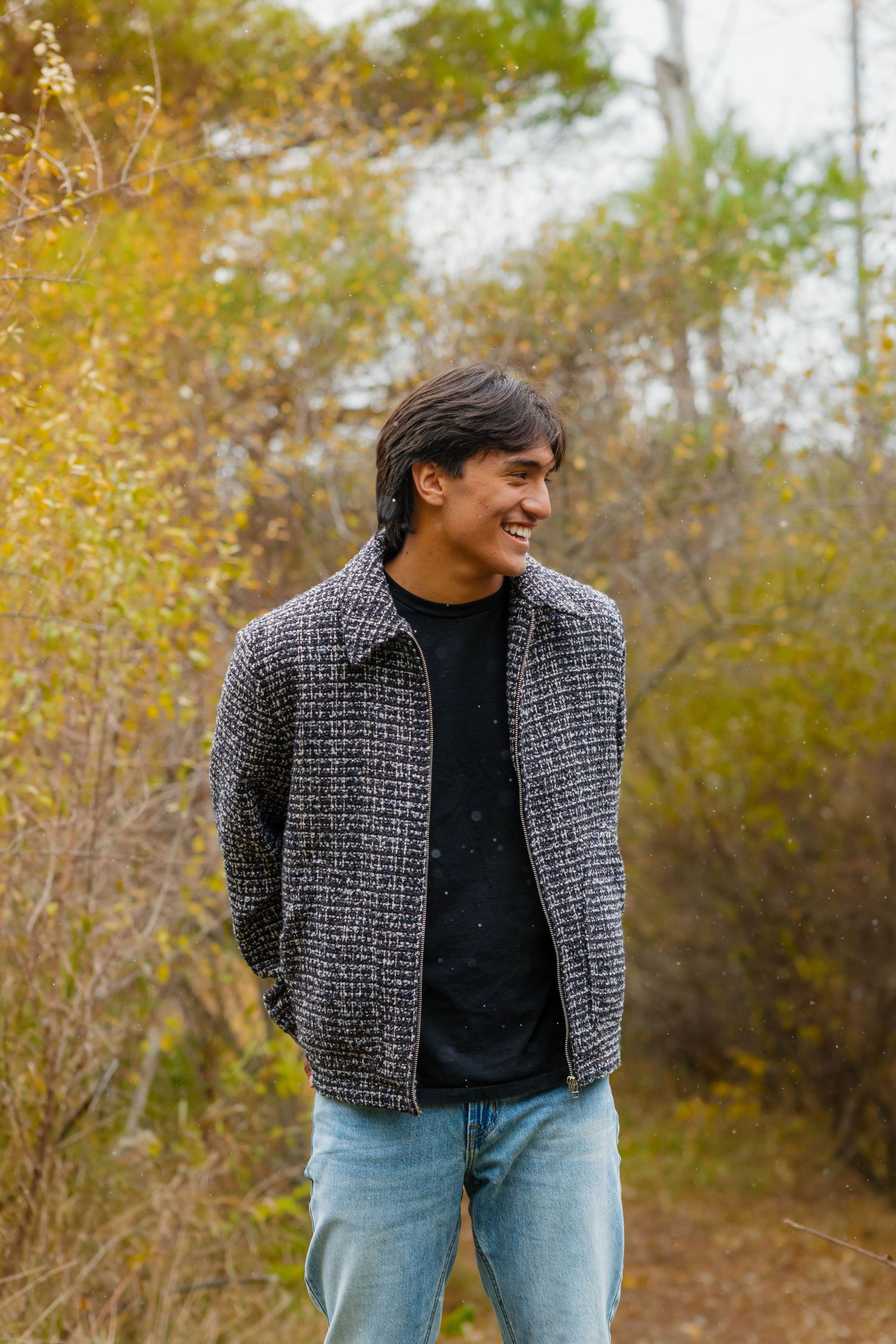 Smiling teen in plaid jacket walks through colorful autumn foliage outdoors.