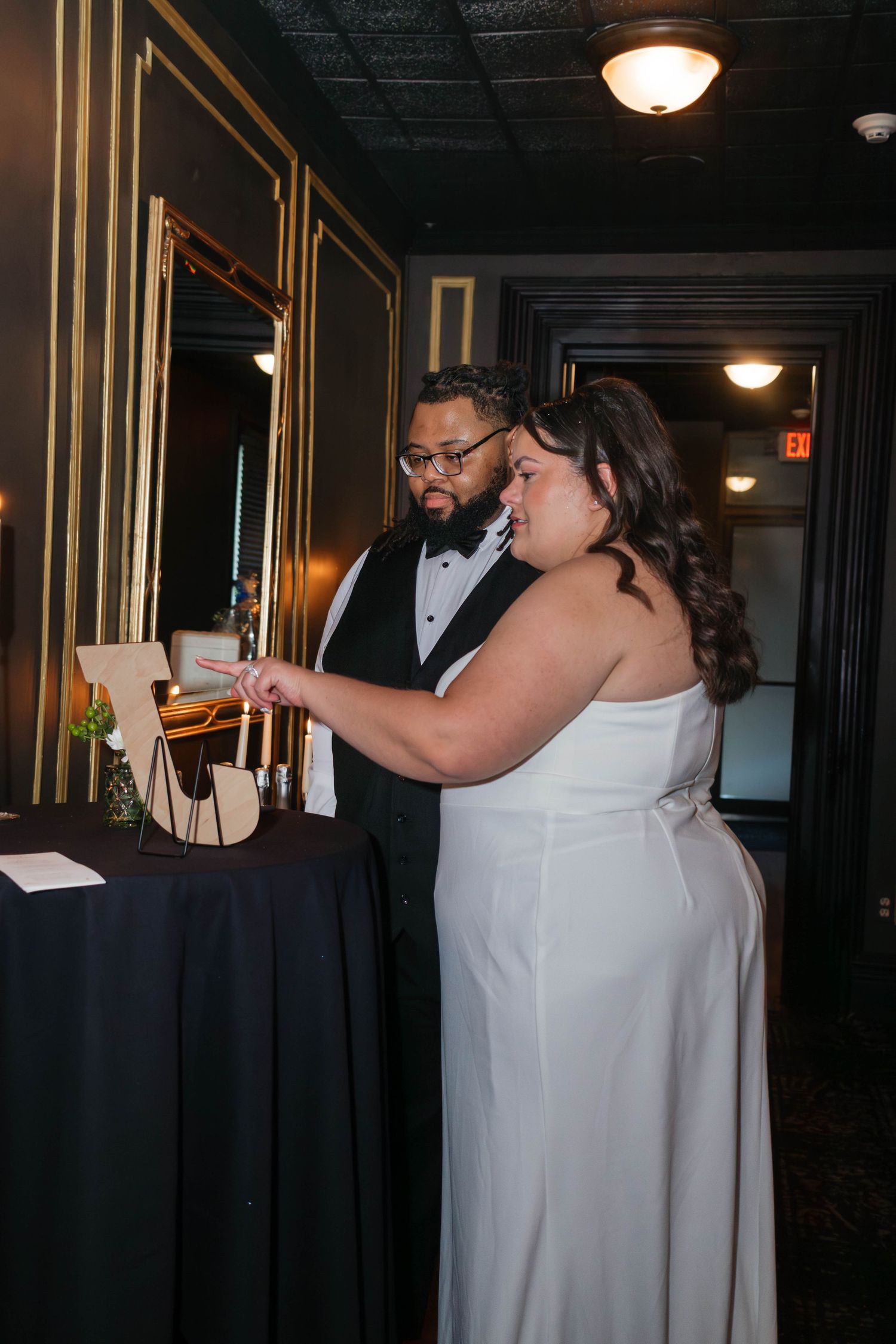 Bride and groom in formal attire examining wedding guest book at decorated reception table.