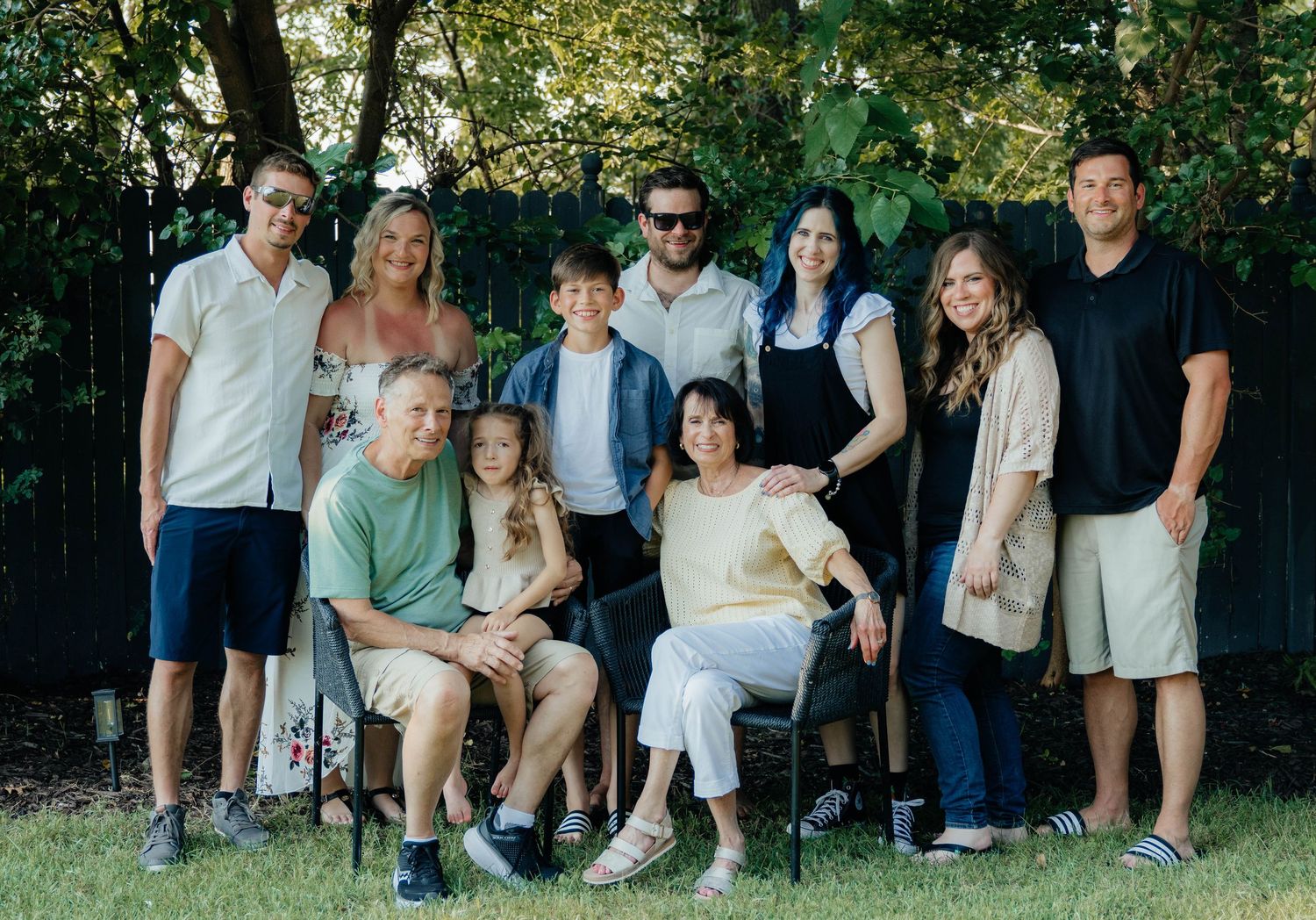 Large extended family group portrait taken outdoors in a backyard with green trees.