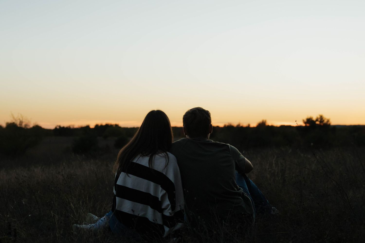 Silhouette of a couple sitting together in a field at sunset.